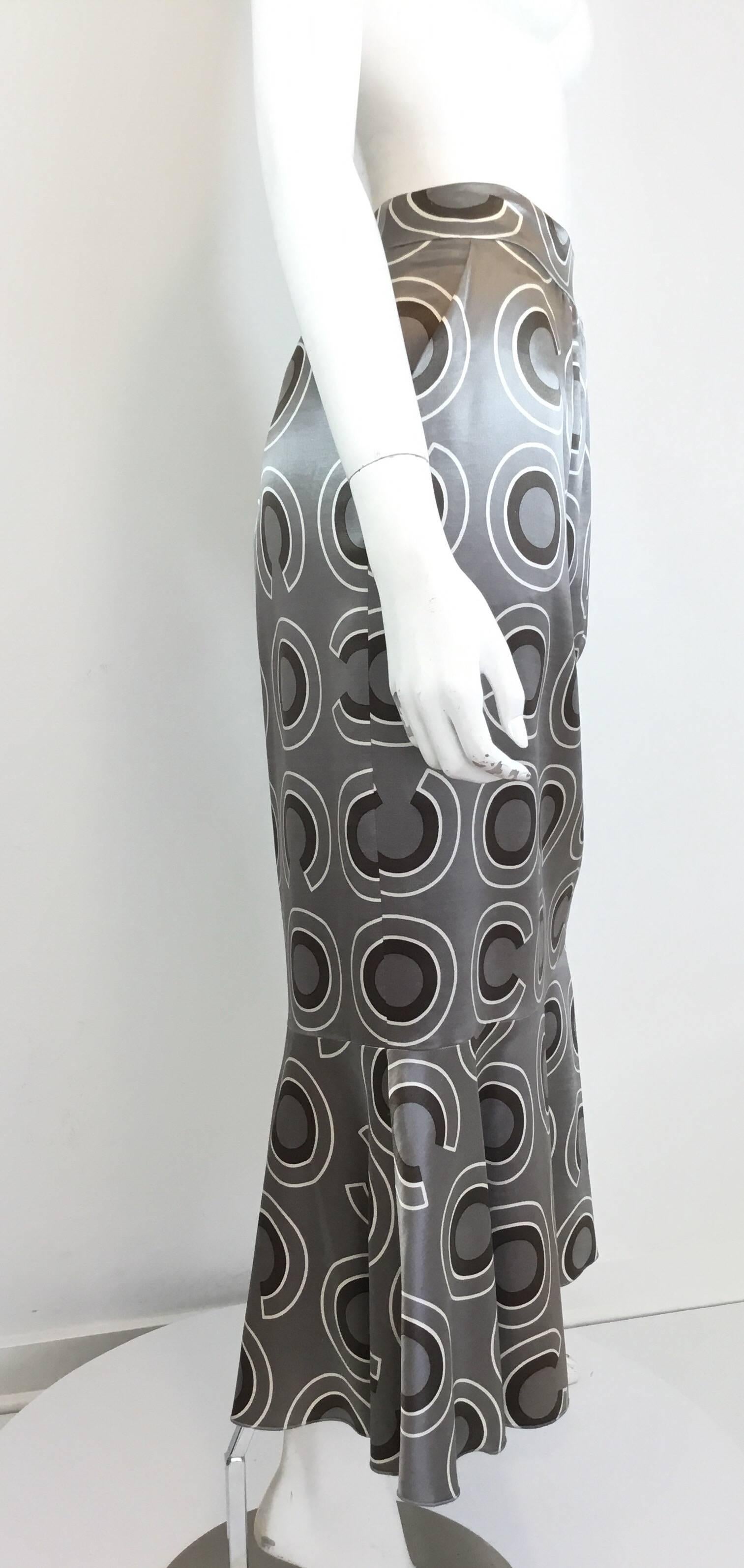 Grey Chanel skirt features a “Coco” Print throughout, pockets at the hip, fluted style with a back zipper fastening. Fully lined. Skirt is labeled Size 44, made in France, Wool/Silk Blend. 

Waist 32”, hips 42”, length 36”