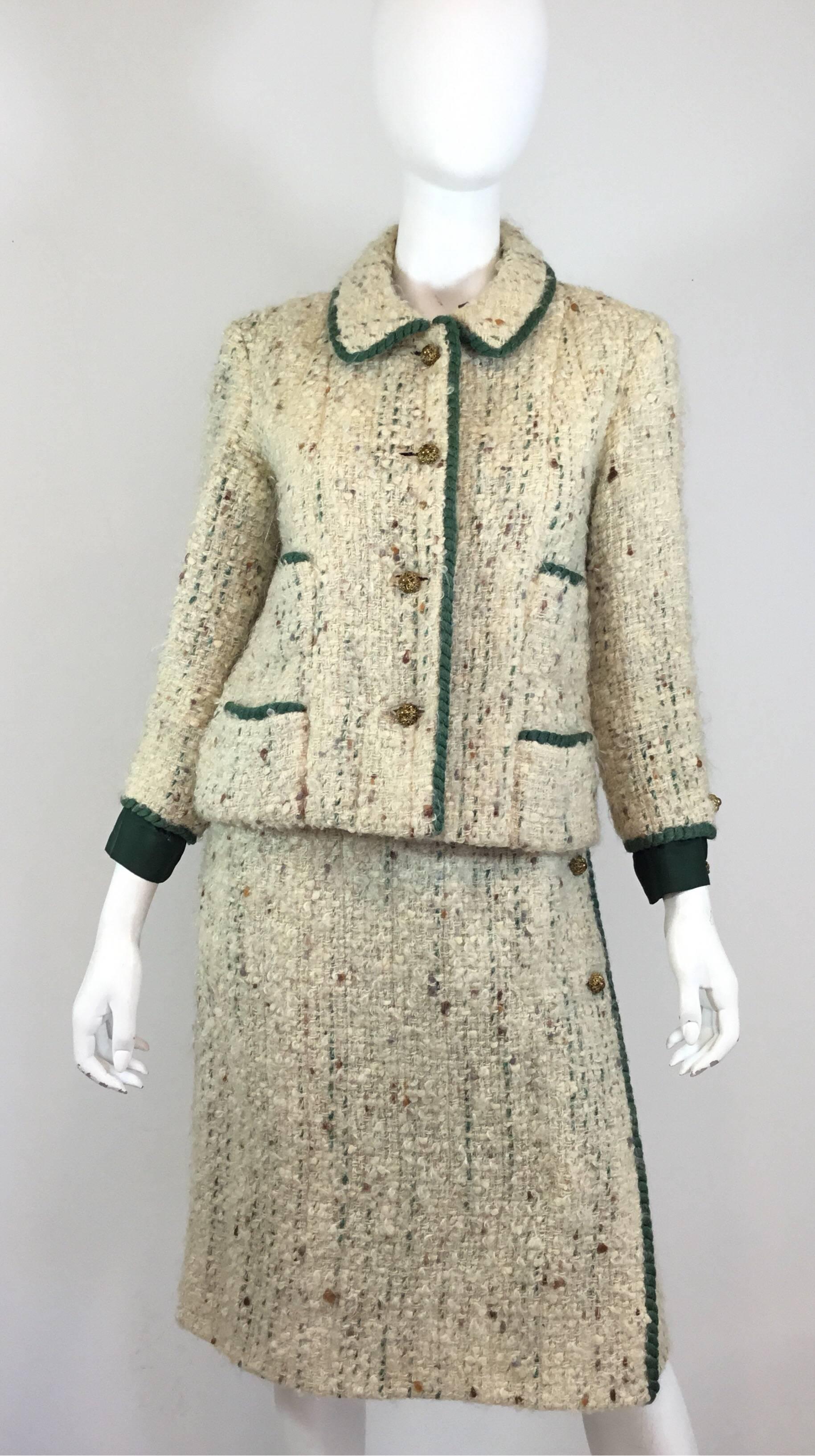 Chanel Couture skirt suit, circa 1950-1960’s. Tweed jacket is featured in an off white tweed knit with a green trim, antique brass hardware button closures, total of four patch pockets, silk cuff and button detail at the sleeves, chain trim along to