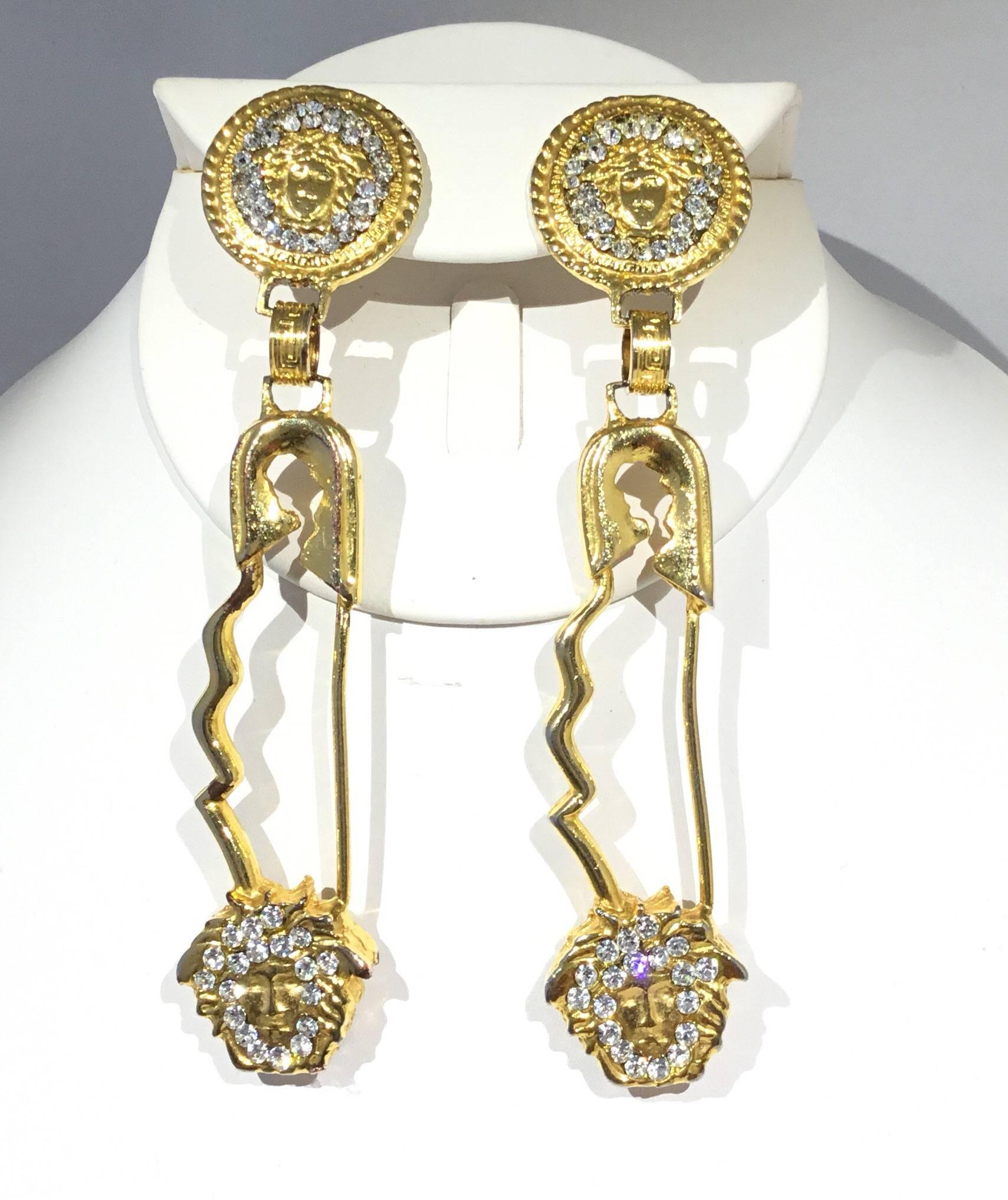 Iconic Gianni Versace vintage 1990s safety pin clip on earrings featured in gold tone with a rhinestone encrusted Medusa head detail. Approximately 4.5 inches long
