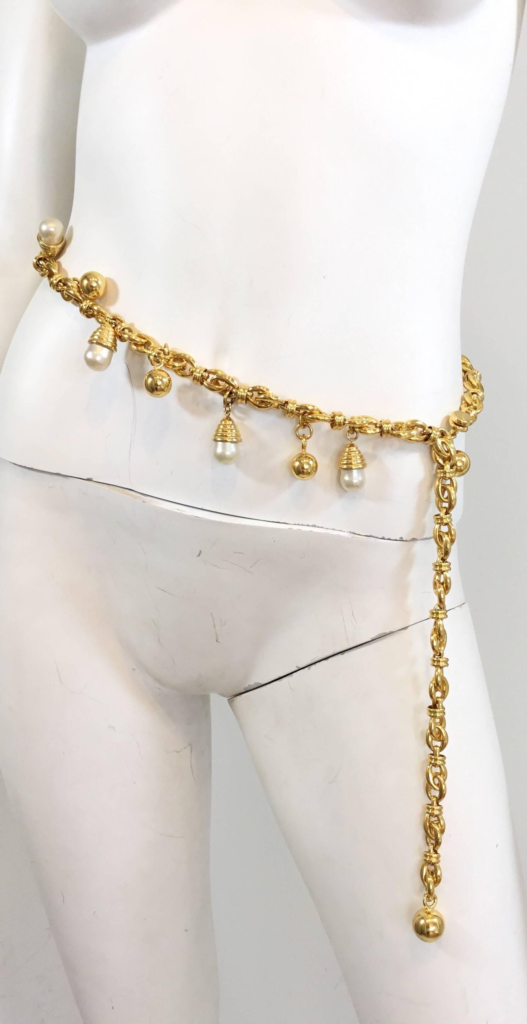 Judith Leiber gold tone chain belt features dangling faux pearls and a hook and eye closure. Chain is approximately 38 inches long. 