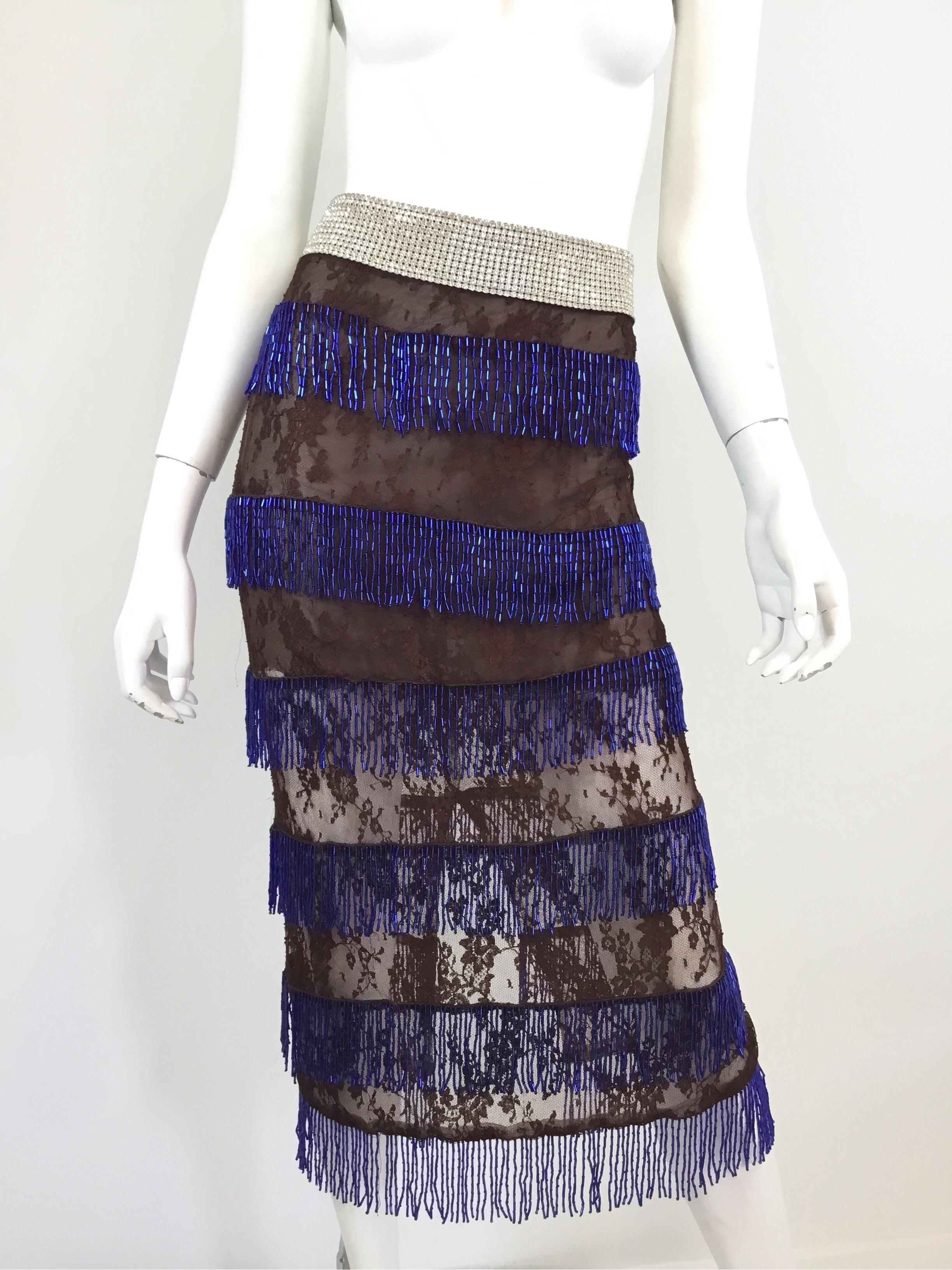 Dolce & Gabbana Brown lace skirt with a rhinestone encrusted waistband and blue dangling beadwork. Skirt has a back zipper closure. Labeled Size 42, viscose and nylon blend, full lining. Made in Italy.

Measurements:
Waist 31”, hips 34”, length 33”