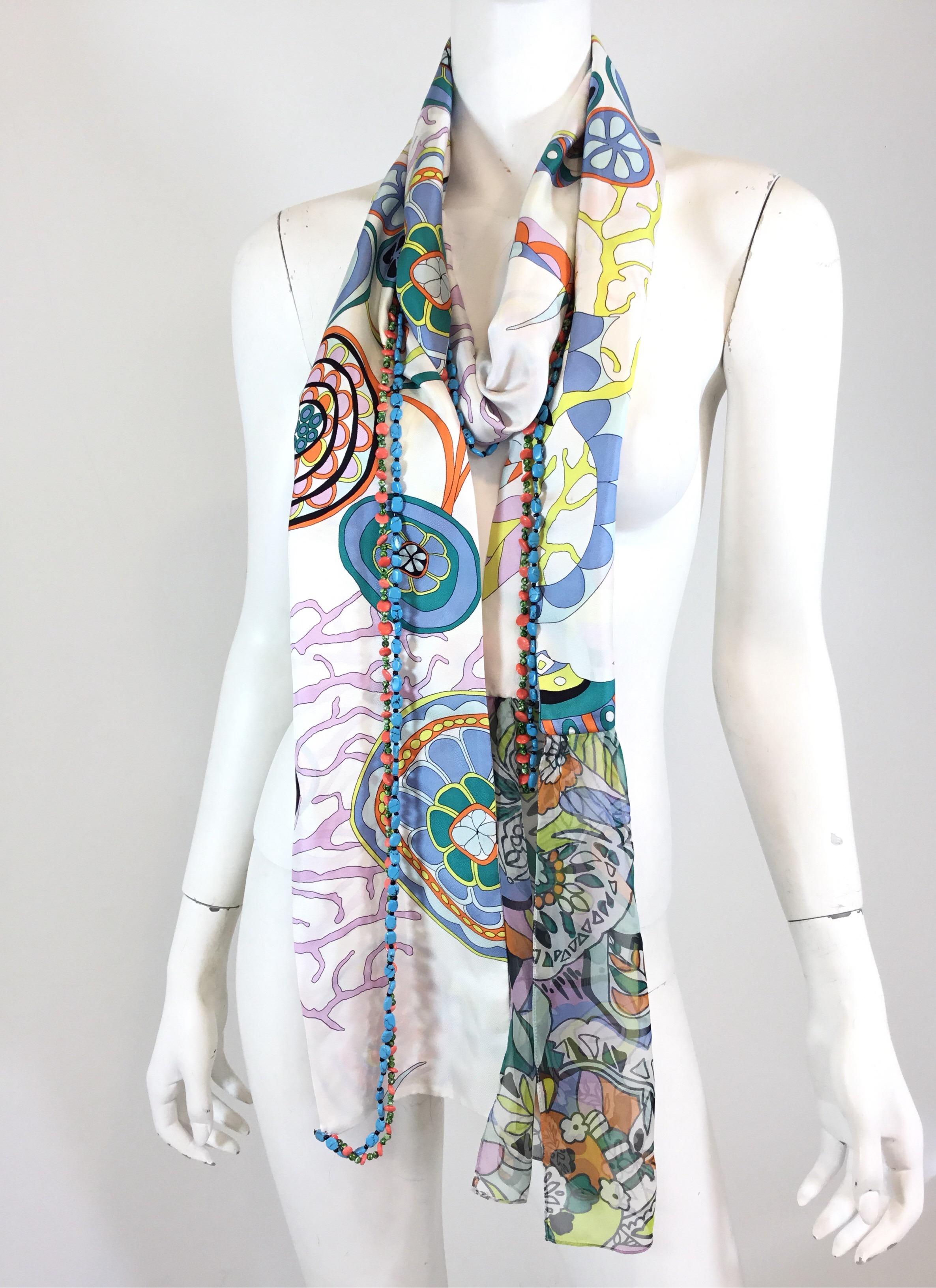Christian Lacroix satin scarf features a multi color print on a white background,  with a sheer trim at one end, turquoise and Coral necklace attached. Scarf measures 90” long. Scarf has few pulls to the sheer trim and a small spot as seen in the