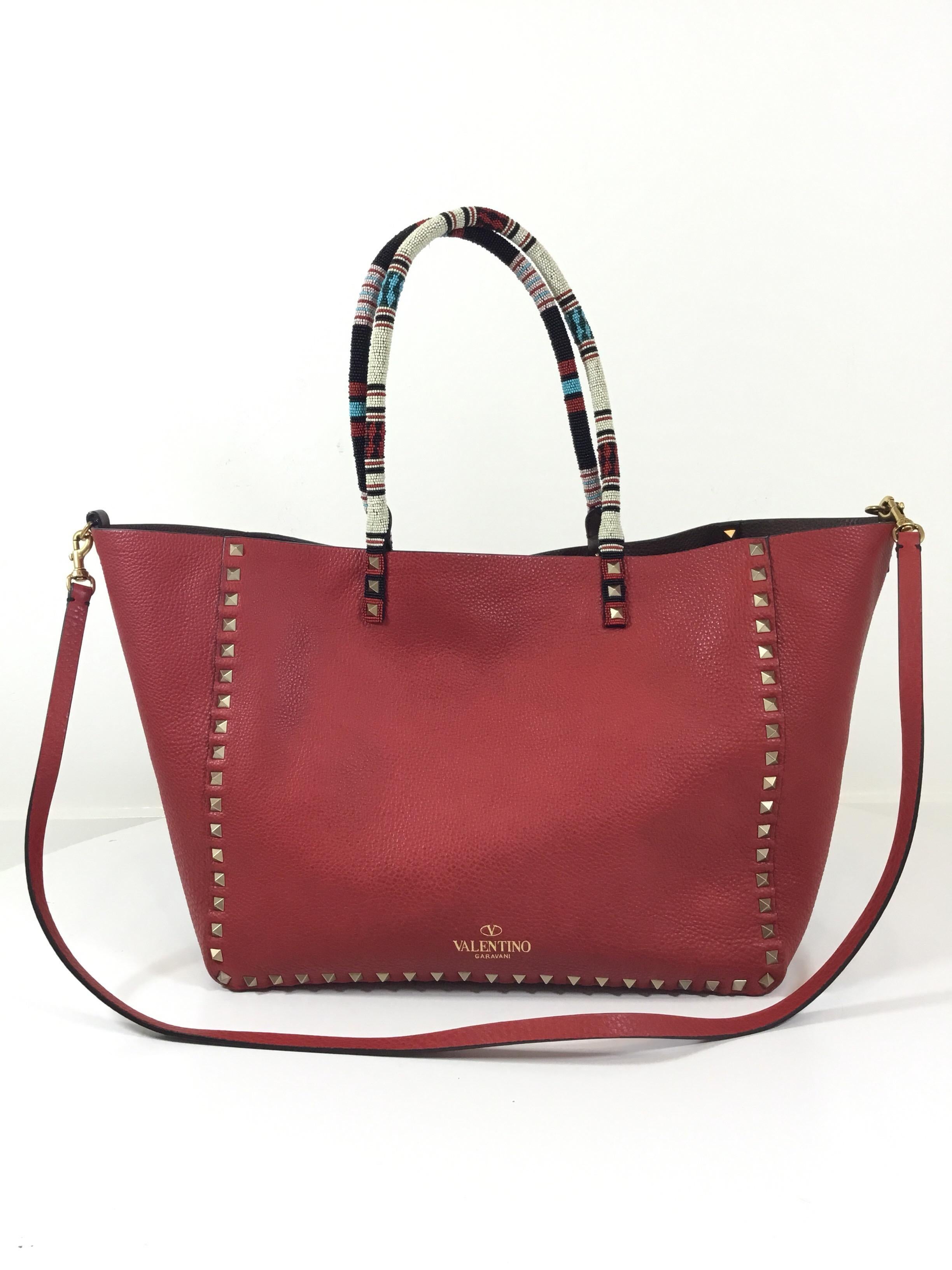 Valentino leather tote for Spring/Summer 2016 Collection inspired by African culture. Tote is featured in medium and is reversible in red and brown with signature rockstud applique along the trim, and fully beaded handles. Tote also includes a long