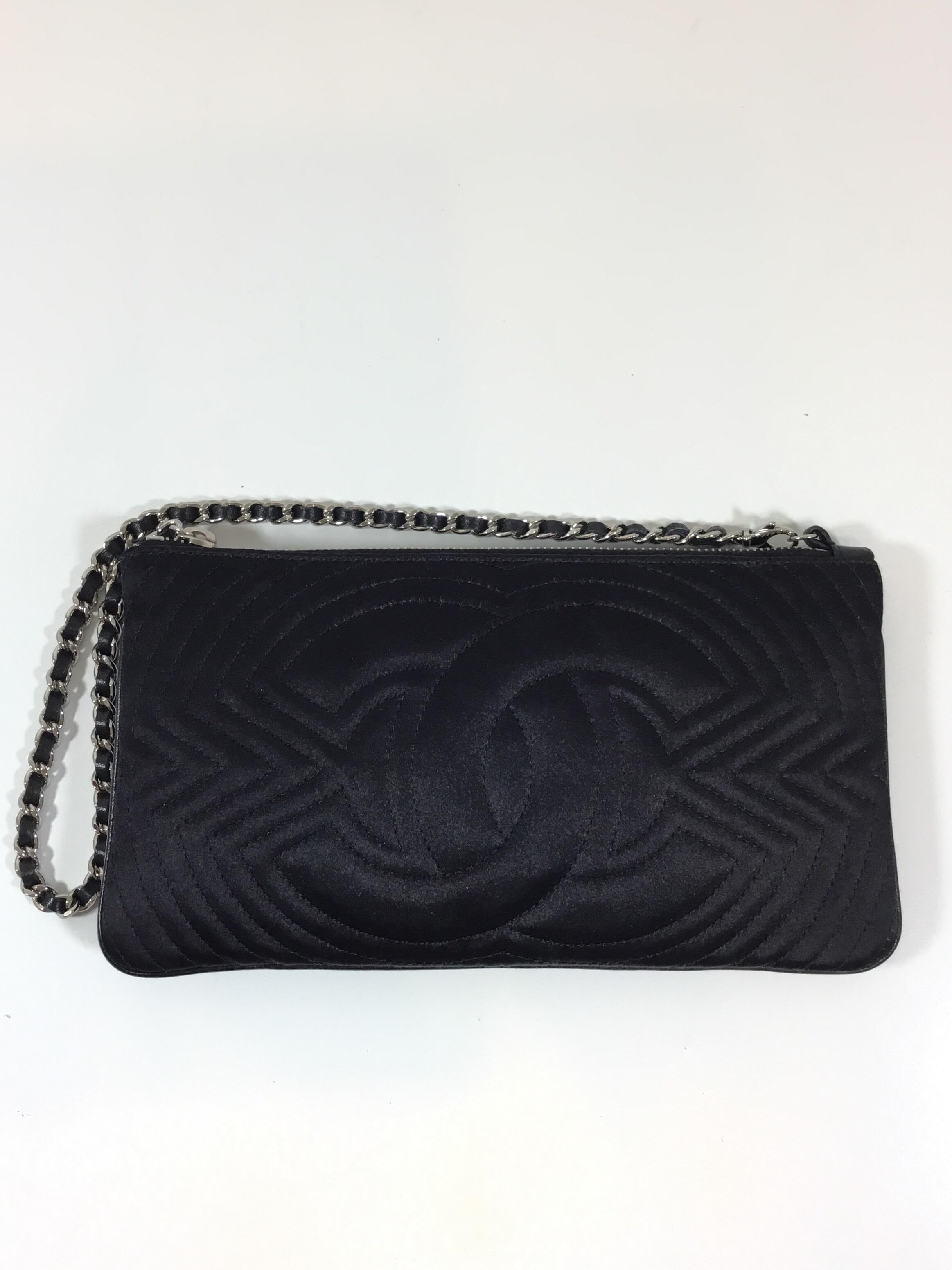 Chanel quilted satin clutch in black with a leather and silvertone chain handle, chain handle has a clip clasp, zipper top closure. Interior is fully lined with a slip pocket. Made in France. Bag includes original dustbag and authenticity card.