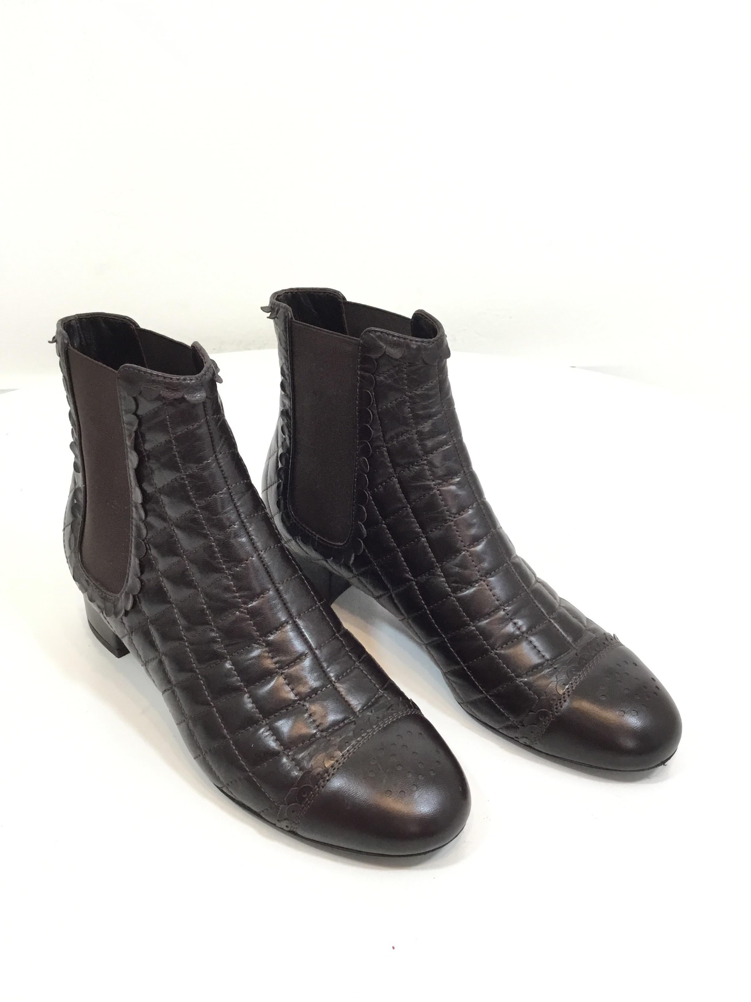 Chanel booties featured in a quilted brown leather with a CC perforated design at the toe and a ruffle-like trim throughout. Booties have stretchy side panels for easy entry. Size 38, made in Italy, leather soles. Shaft 5”, heel 1.5”. Normal wears
