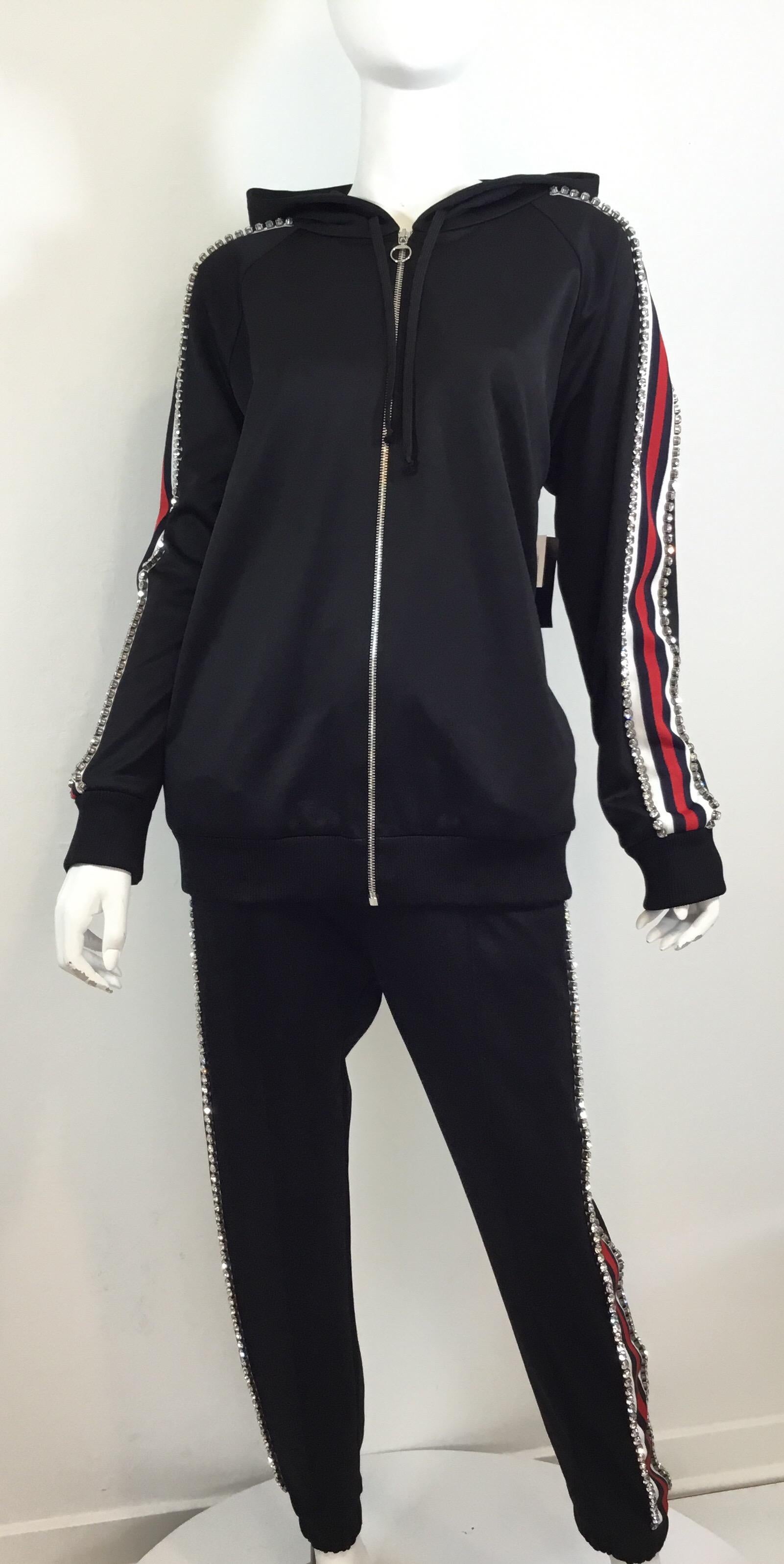 Gucci tracksuit featured in a black tech-jersey fabric with a red and navy web panel along the sides encrusted with Swarovski crystals. Jacket is hooded and has a zippered fastening. Pants have a drawstring fastening at the waist and gathered