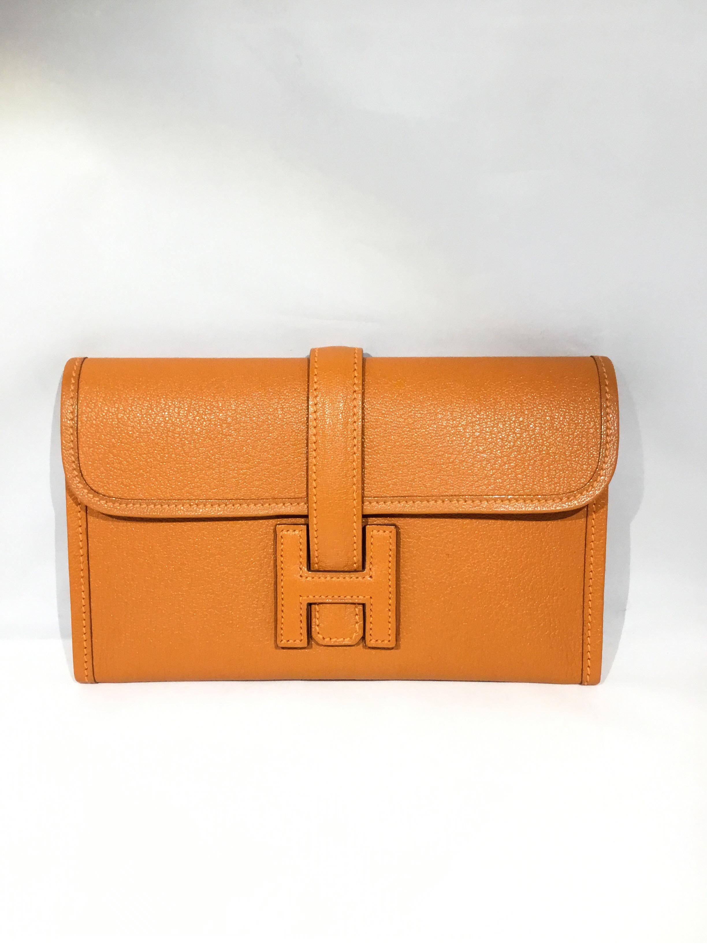 Hermes 20cm Jige clutch is crafted of textured goatskin leather in a burnt orange. The cross-over flap and strap secures under a leather Hermes H. Made in France. 

Box + Dustbag included

Blind Stamp: P K in a square, 25

Measurements: 8” x 1” x 5”