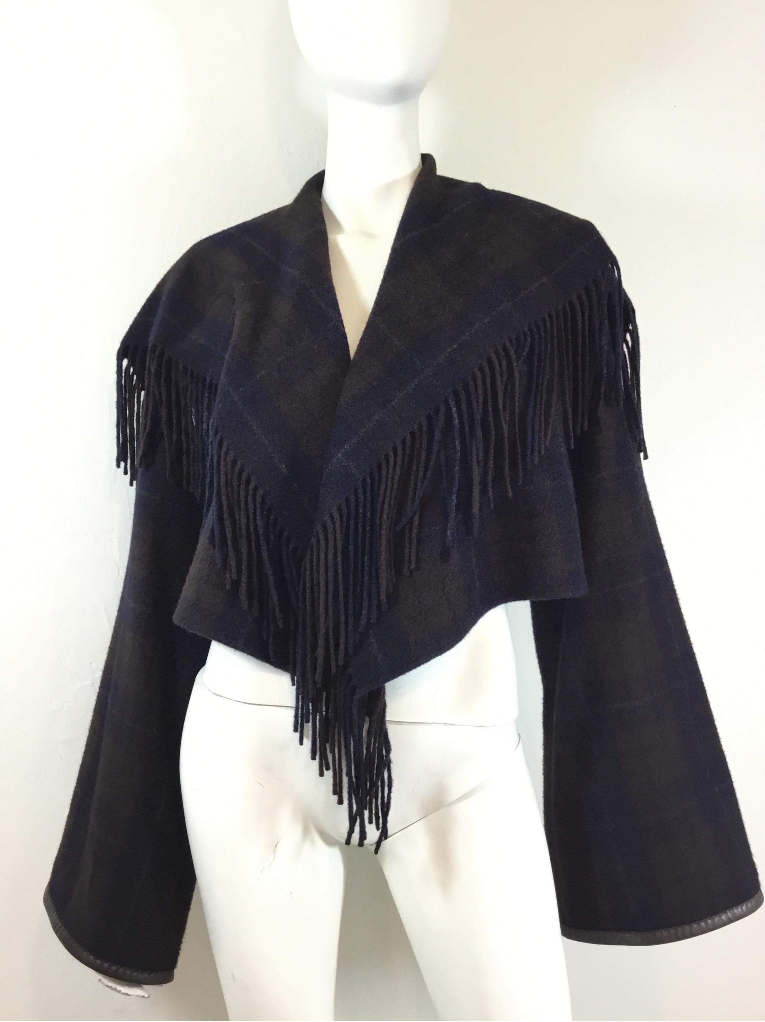 Hermes capelet features a plaid pattern throughout with a leather and fringe trimming, wide bell sleeves, and is composed of 100% cashmere. Size 34, Made in France. Excellent condition.

Bust 36”, sleeves 27”, length 19”