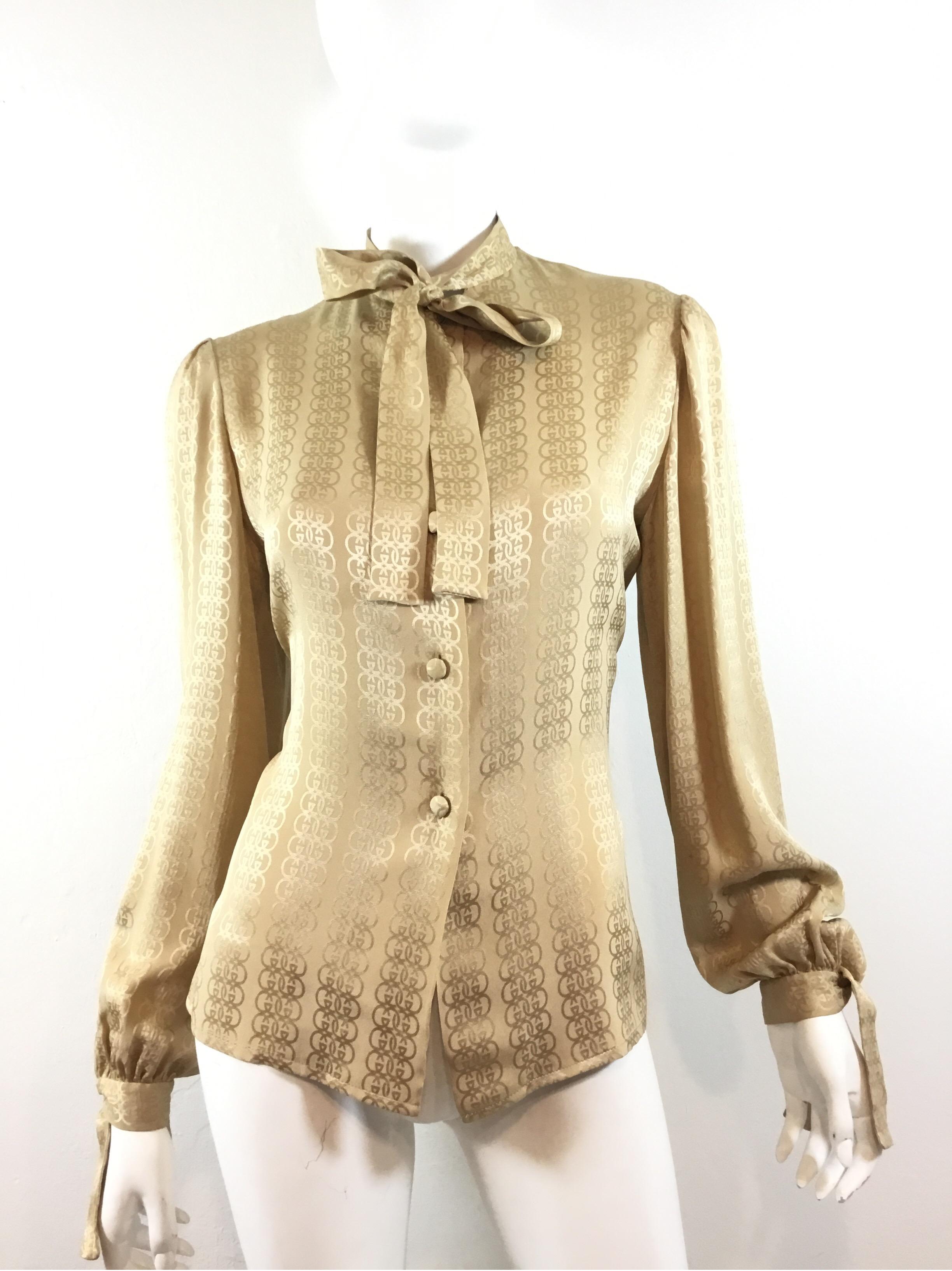 Gucci silk blouse featured in a beige/tan color with the signature GG monogram throughout. Blouse has button fastenings along the front and on the cuffs, and has an attached neck tie. 100% silk, labeled size 48, made in Italy. Excellent
