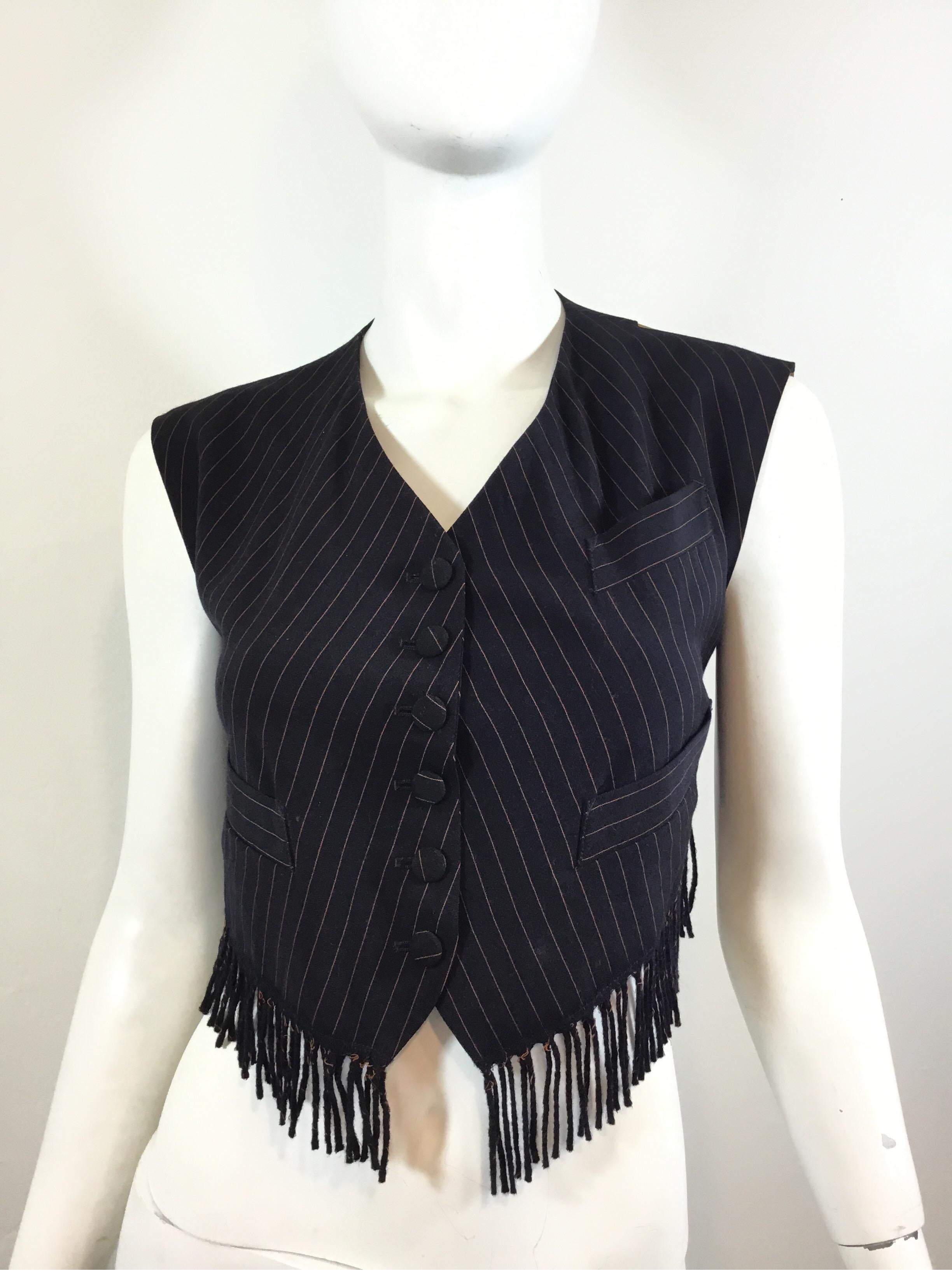 Jean Paul Gaultier vest featured in navy with a pinstriped pattern throughout and a fringed hem. Vest has 3 functional pockets and button closures at the front and an adjustable strap at the back. Labeled Size 46, made in Italy.

Bust 38”, length 14”