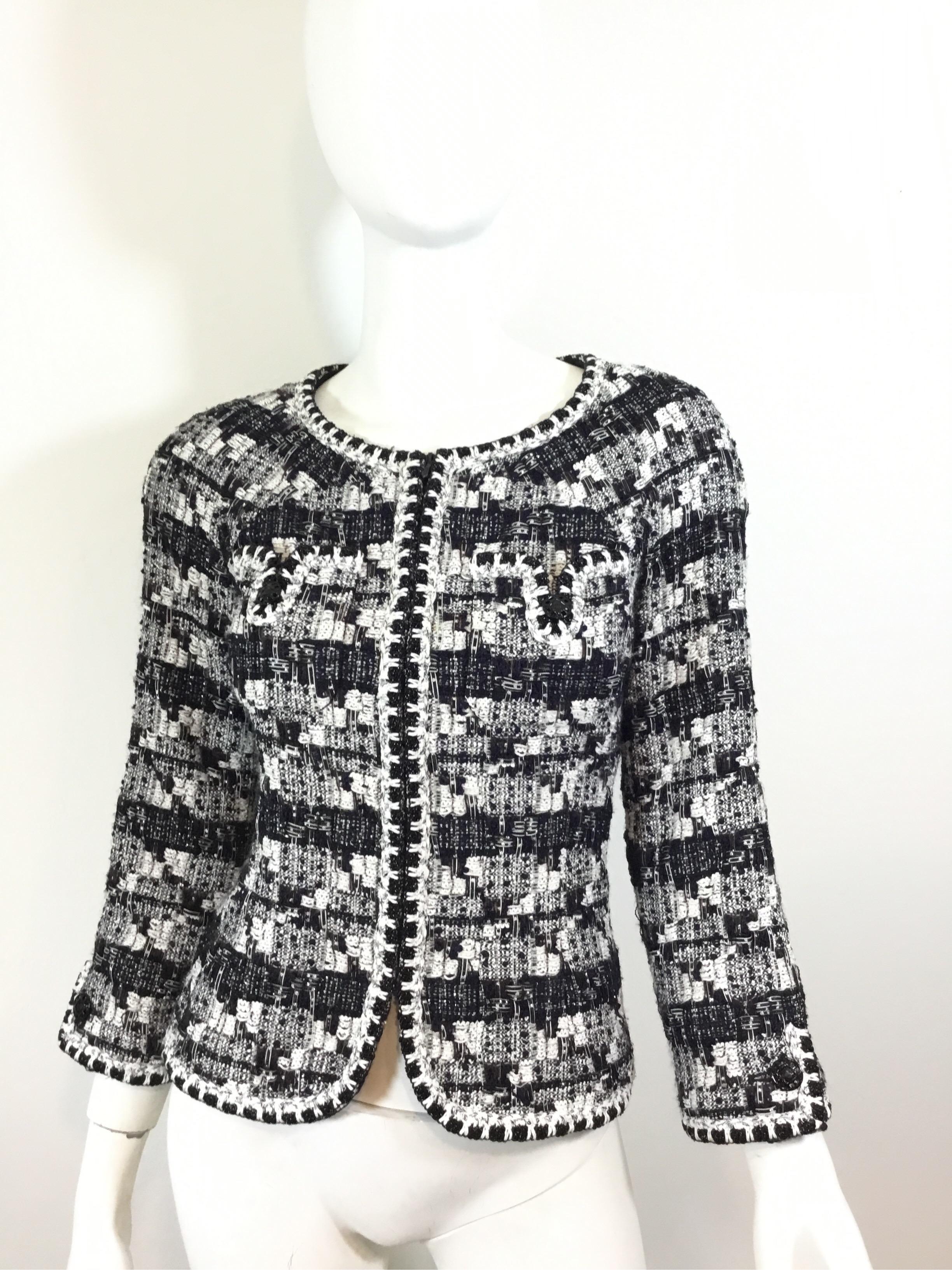 Chanel tweed jacket in black, navy, and white tweed knit throughout, black beading along the trim of the jacket, zipper fastening, full lining with a chain trim along the hem, and two buttoned pockets at the bust. Jacket is a size 36, made in