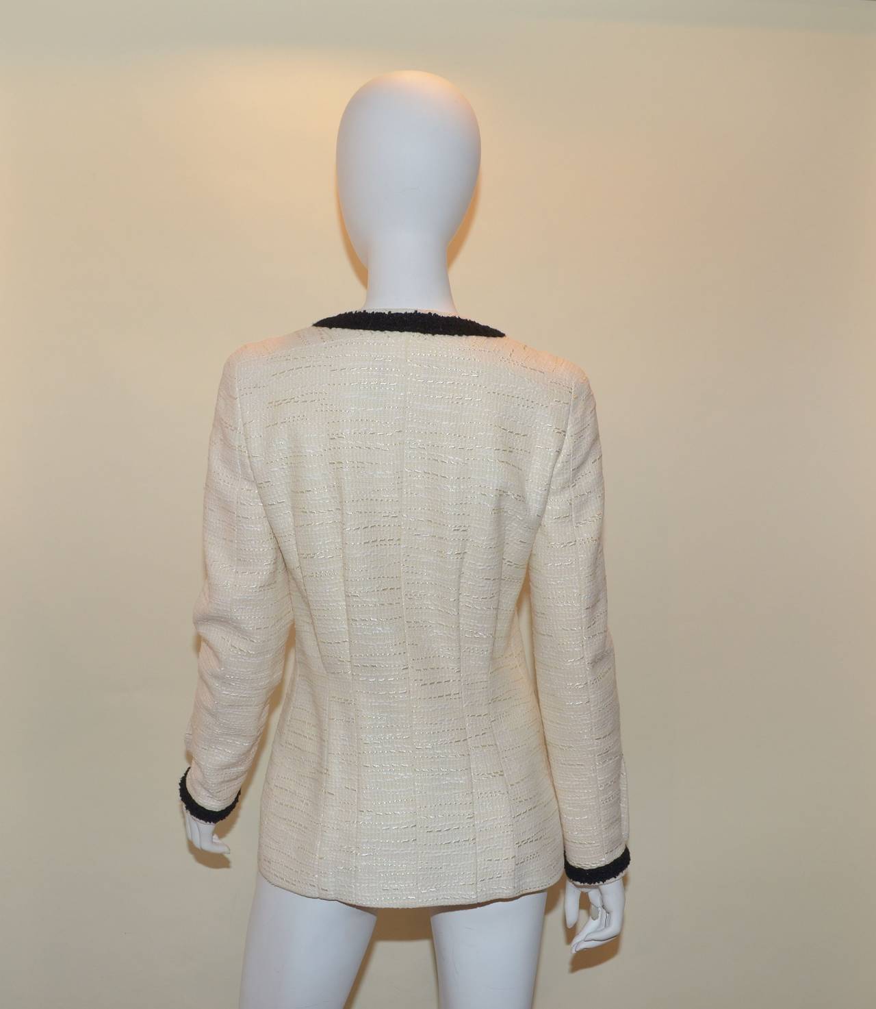 Classic Chanel jacket features a cream-colored boucle knit with a black trim for great contrast. Jacket has a front zipper closure, Euro sign buttons with cc logo and euro sign along the cuff, pin-tucking at the back center, and 2 slip pockets at