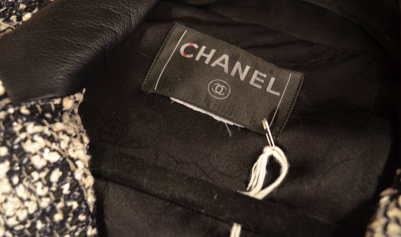 Chanel blazer features a houndstooth design throughout the signature tweed fabric, black leather trimmings along the cuffs and pockets, leather trim at the collar as well. Silver metallic threads in the tweed. Concealed silver-tone CC button