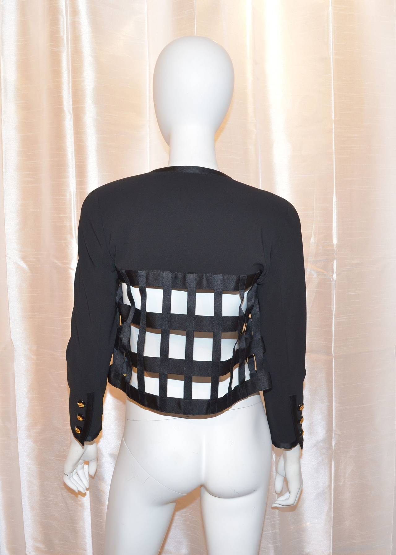 Chanel jacket features a cutout satin ribbon caged bodice. Jacket is open with no button closures and there is a chain trim along the inside of the hem. Buttons at sleeves. From the 1992 fall winter collection. Made in France, size 38. Made with 94%