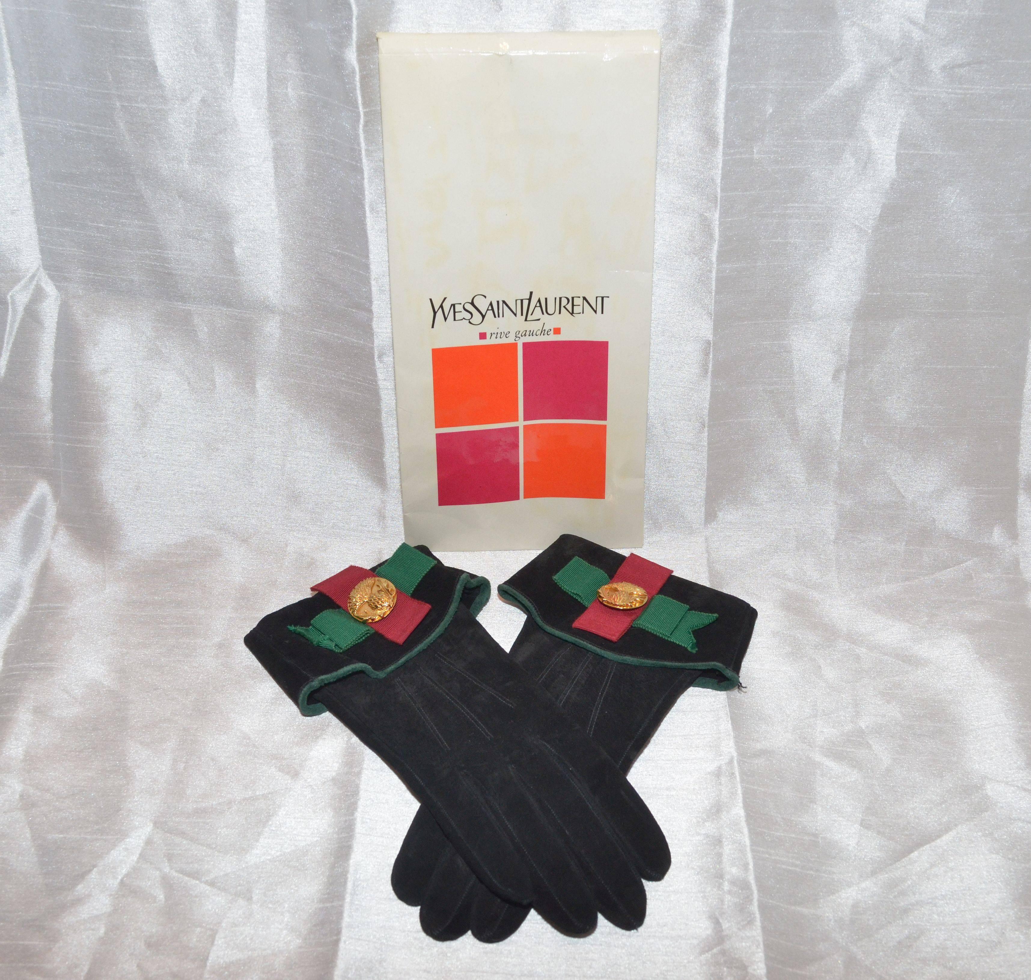 Yves Saint Laurent gloves in suede leather with red and green ribbon detail and a gold-tone metal center applique at the opening. Gloves are labeled a size 6.5 and Made in France. Gloves include original packaging.

Opening length - 4.5''