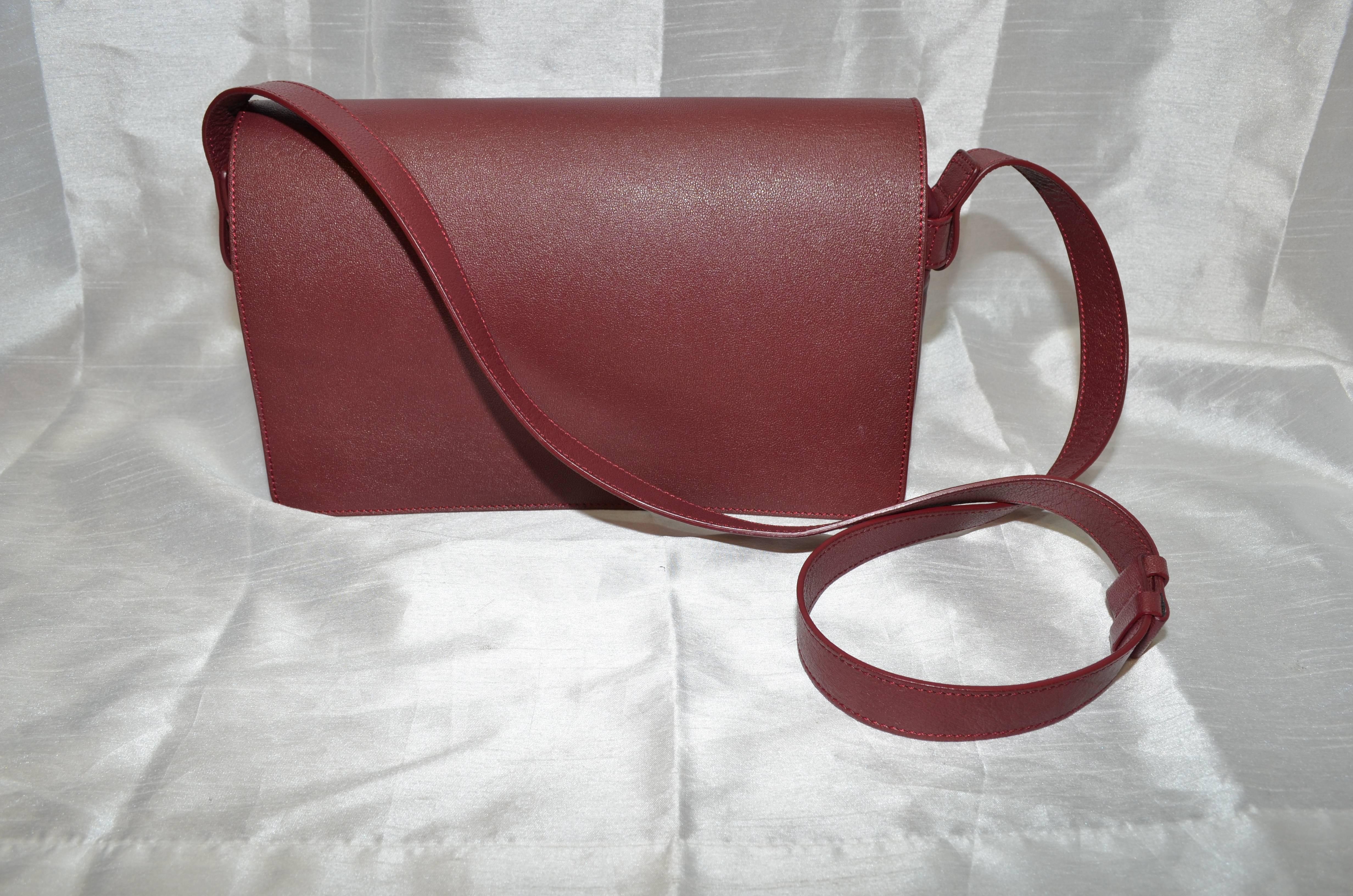 Margiela bag is featured in maroon leather with a flat shoulder strap, exposed stitches for a label on the back side. Structured outer-shell with a relaxed zip top center compartment, flap front with a snap stud closure, and one pocket underneath