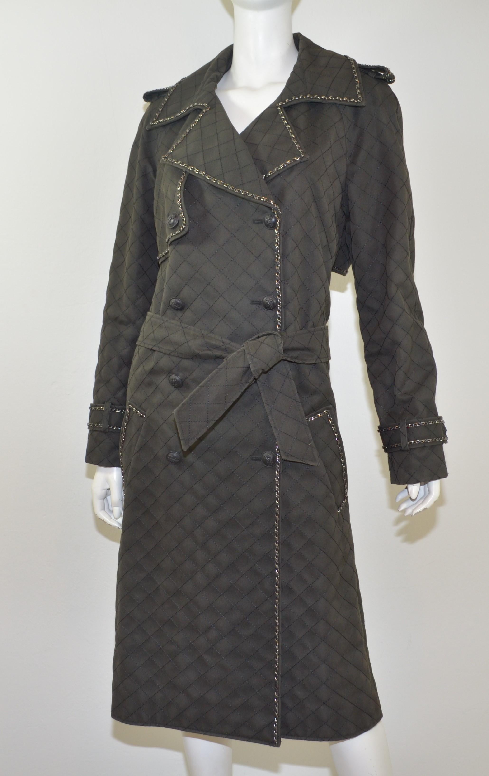 Beautiful Chanel trench coat featured in a dark green/grey color with silver tone and leather intertwined chain trim throughout, pewter buttons with signature CC insignia. 100% silk full lining. Waist tie and button fastening, size 44, made in