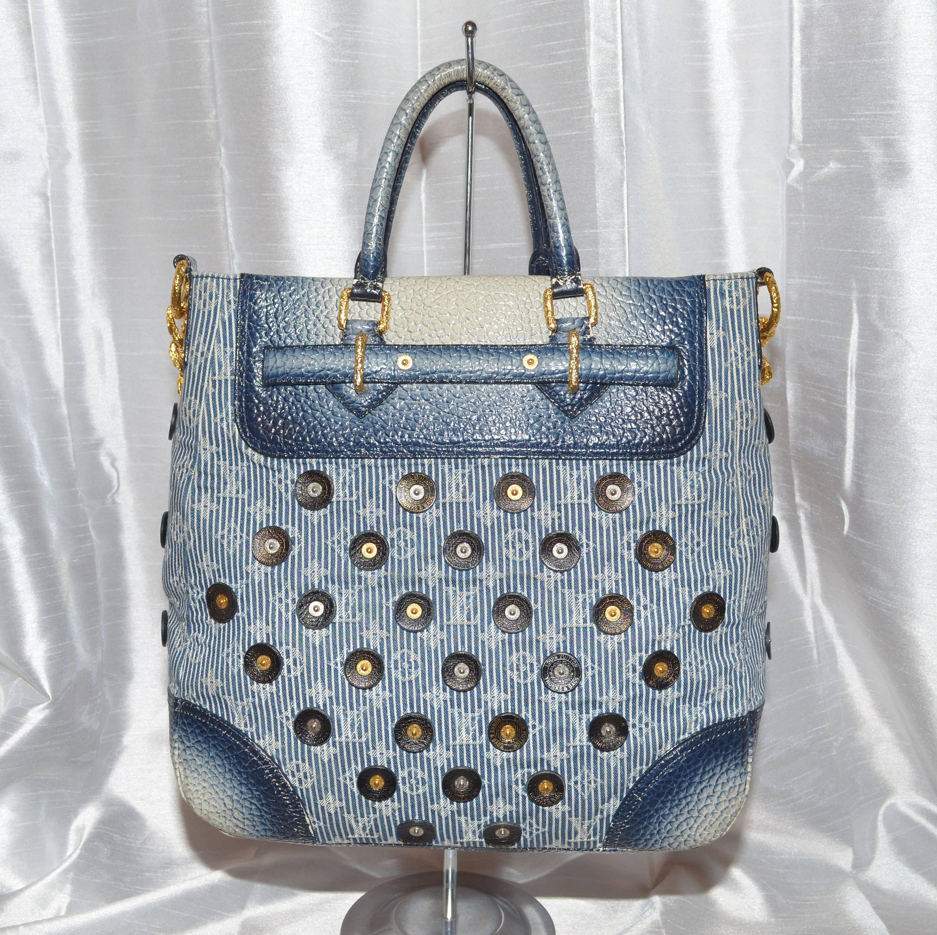 Louis Vuitton tote features a denim monogram fabric throughout with leather and gold-tone metal applique. Two top rolled handles, thick gold chain-link shoulder strap, and a pebbled leather base. Decorative padlock with functioning keys. Interior is