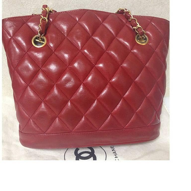 1980s. Vintage CHANEL lipstick red quilted lamb leather trapezoid shape tote bag with a gold CC plate and chains.

This is a vintage lambskin CHANEL in hot color of red with gold-tone logo plate pull to the zipper from the 80's. The zipper from the