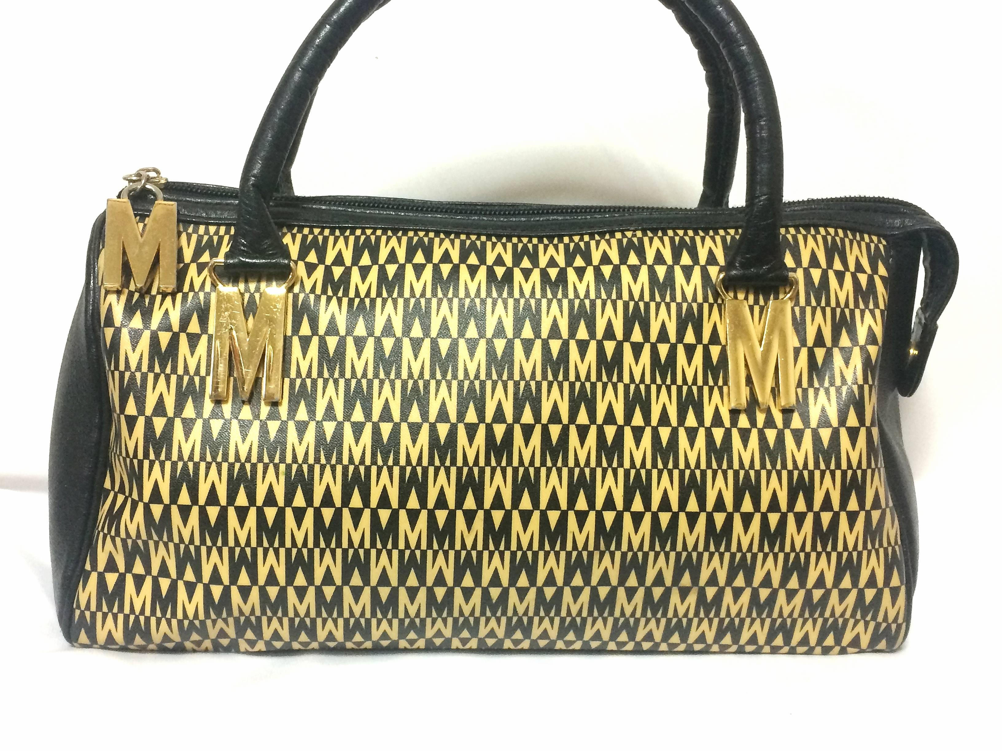 1990s. Vintage MOSCHINO black and ivory beige logo M print handbag, mini duffle bag with leather trimmings and golden M charms.

Introducing a chic and cute vintage piece from Moschino in the 90's!
Rare vintage MOSCHINO bag.
You will love the black