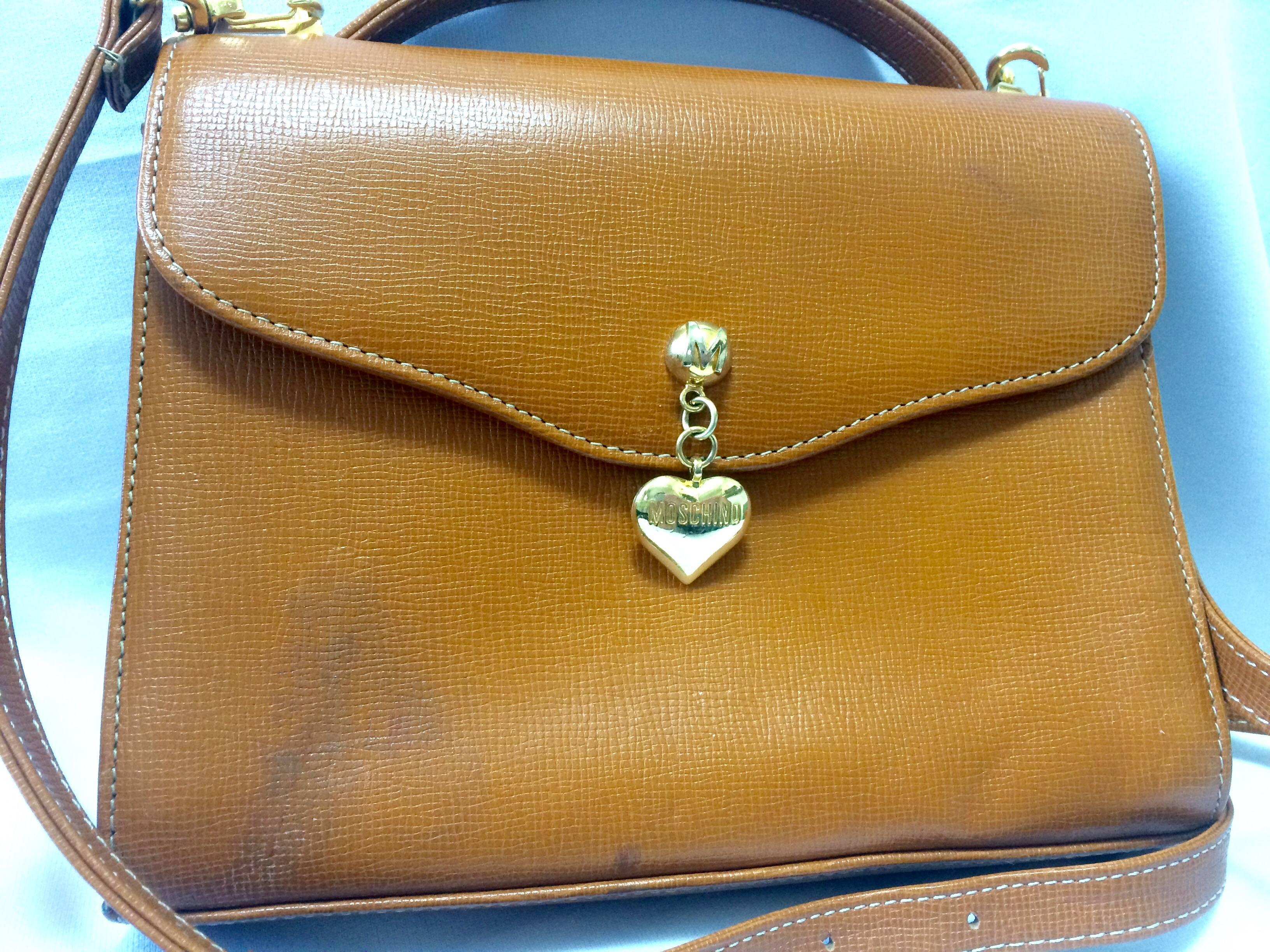 1990s. Vintage MOSCHINO orange brown grained leather kelly handbag with a detachable shoulder strap and golden heart shape logo charm.

Introducing another cute and chic vintage MOSCHINO handbag in orange brown leather bag.
Featuring a golden heart