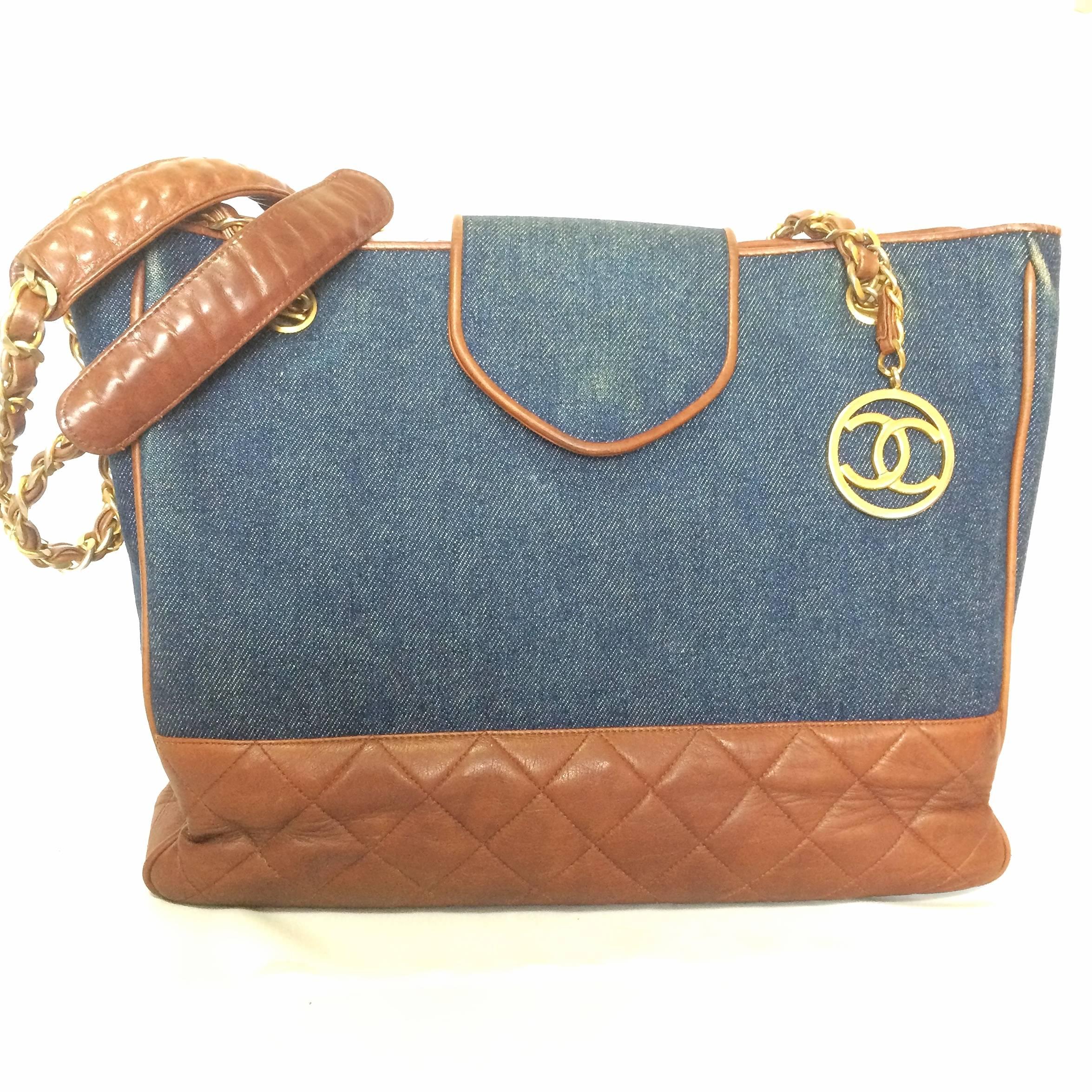 1990s. Vintage CHANEL blue jean denim and brown leather combination classic shopper, shoulder tote bag with golden cc round charm.

Introducing a vintage CHANEL denim fabric and brown goat leather combi tote bag with its iconic gold tone chain