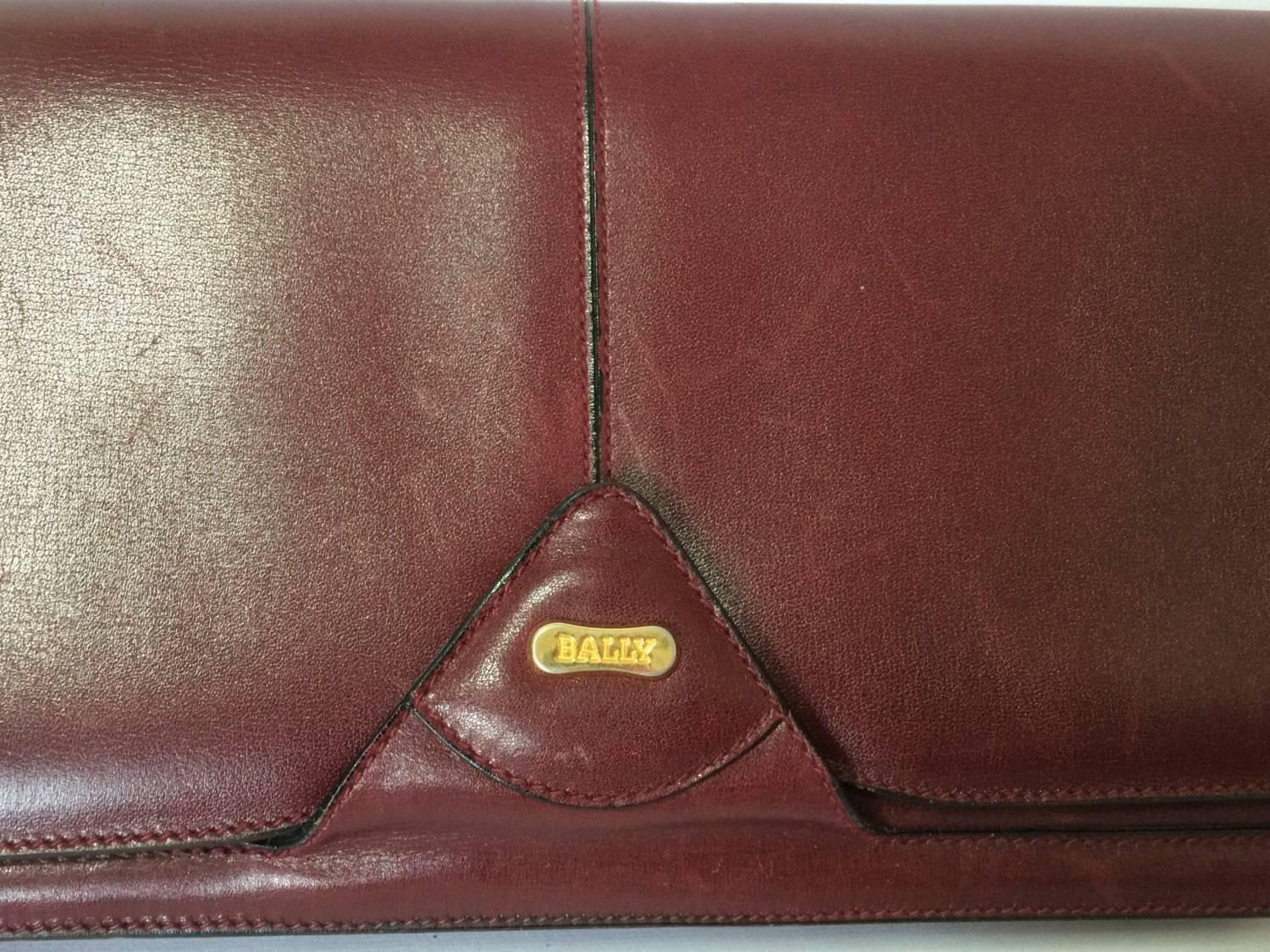 1980s. Vintage Bally wine leather clutch bag, party and classic purse with gold tone logo motif. Unisex use.

Introducing another masterpiece vintage purse from BALLY back in the 80's. 
Classic wine color leather.
Featuring a golden embossed