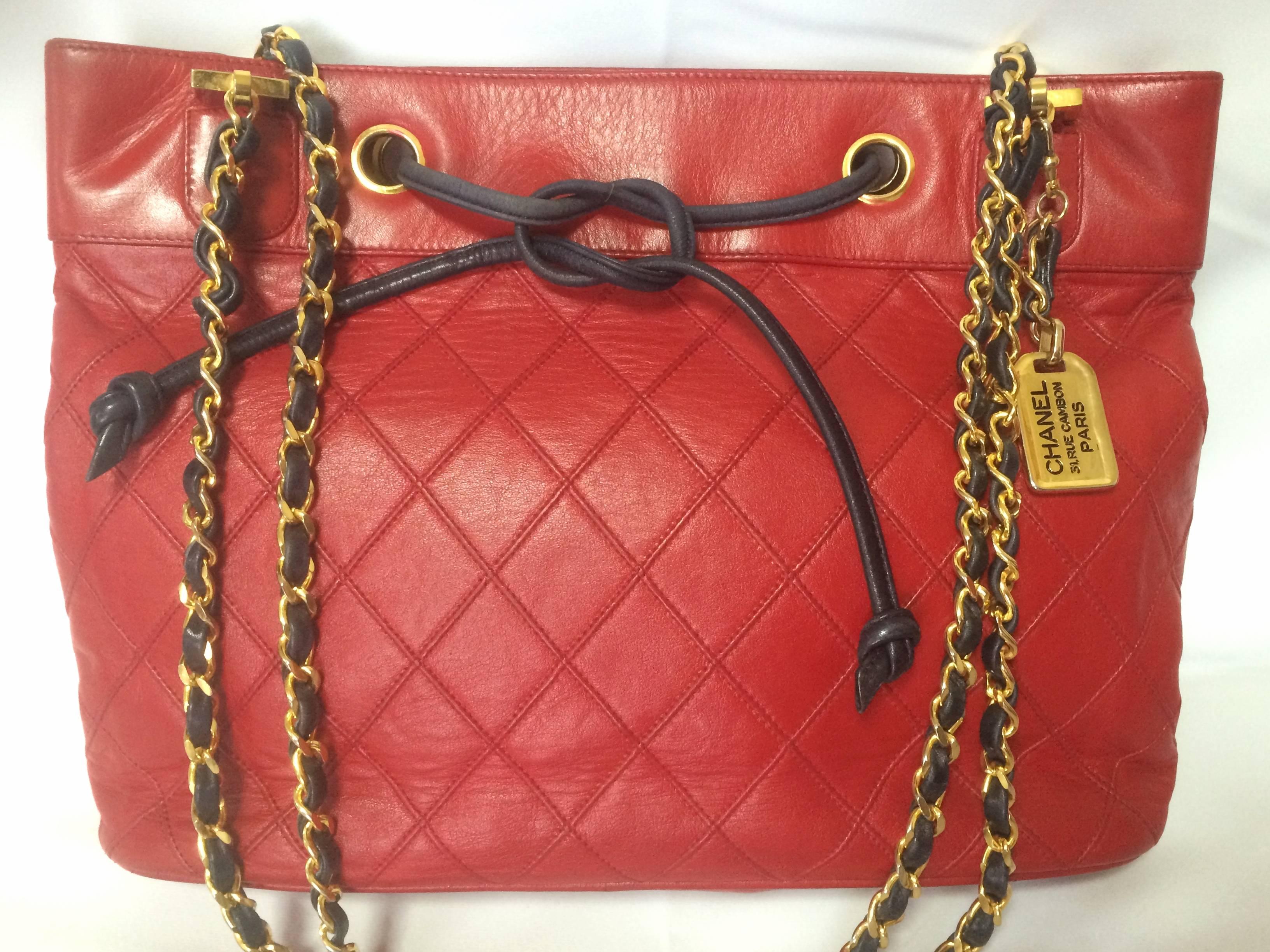 1980s. Vintage CHANEL classic tote bag in red leather with gold tone chain and navy blue leather straps and logo CC charm plate. Rare bag

Vintage Chanel lipstick red calfskin chain shoulder tote bag with navy drawstrings and golden square CC