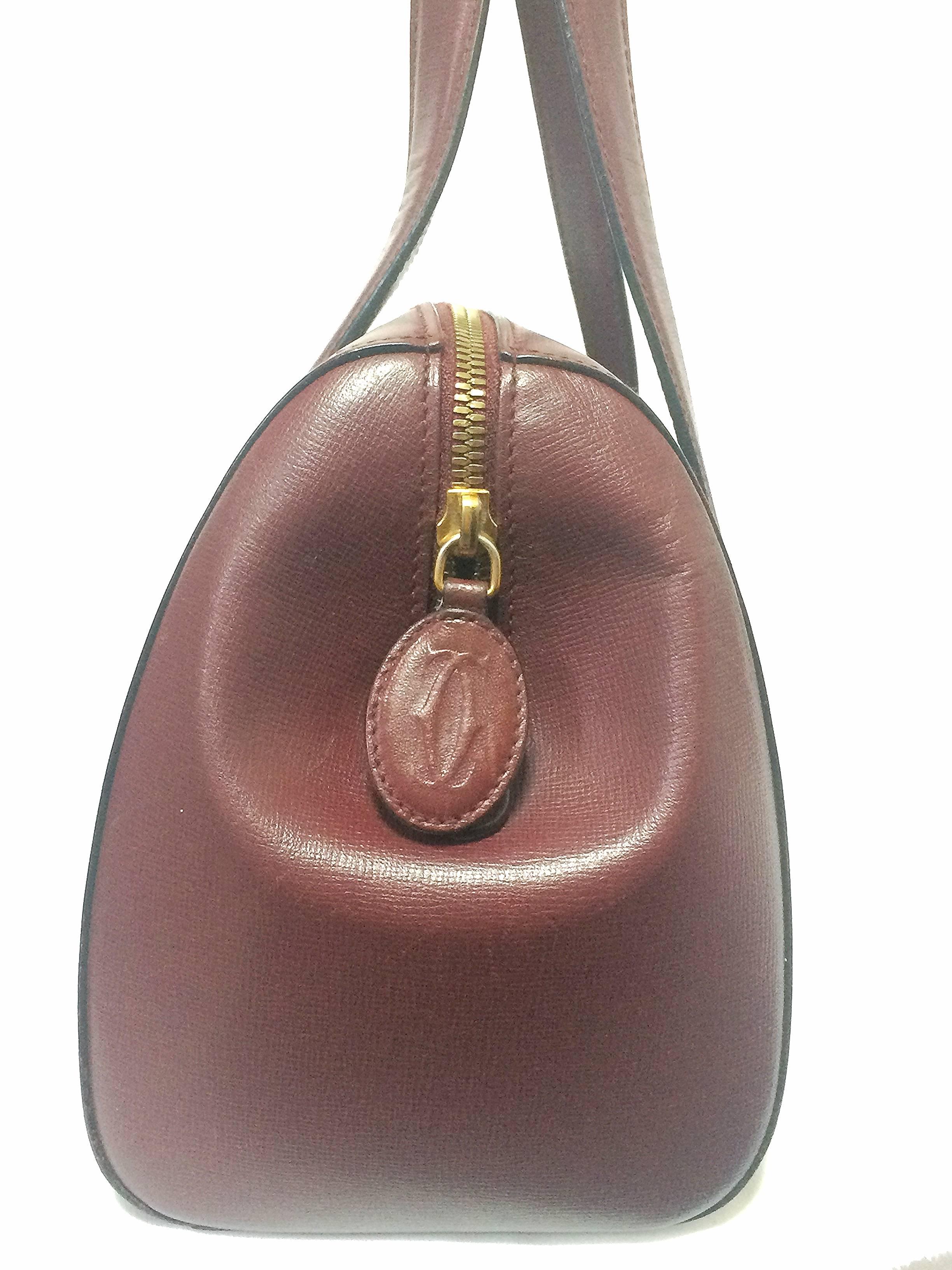 1990s. Vintage Cartier classic wine, bordeaux leather handbag purse in unique shape with bullet design gold hardware at handles. Must de Cartier.

Introducing another vintage masterpiece from Cartier, wine leather purse. 
Has the logo embossed