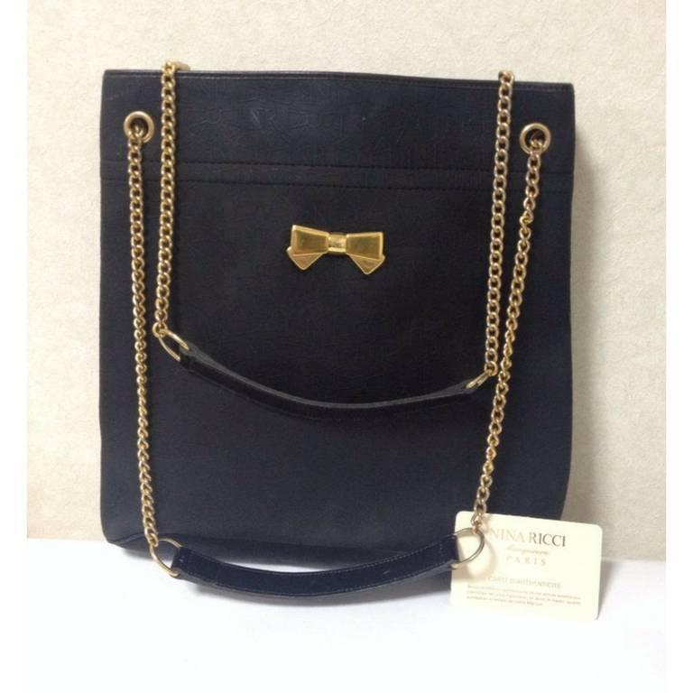1990s. Vintage Nina Ricci black tote bag with golden chain straps with golden logo bow, ribbon shape motif. Perfect daily purse.

Introducing a vintage Nina Ricci shoulder bag, tote bag in classic black color. 
Featuring the logo and ribbon marks
