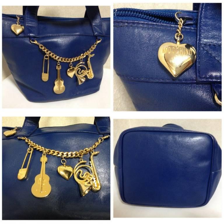 1990s. Vintage Moschino navy blue leather classic tote bag with golden cute dangling charms. Masterpiece jewel bag.

Introducing a chic and cute vintage piece from Moschino back in the early 90's!
Featuring cutest golden charms of heart, guitar,