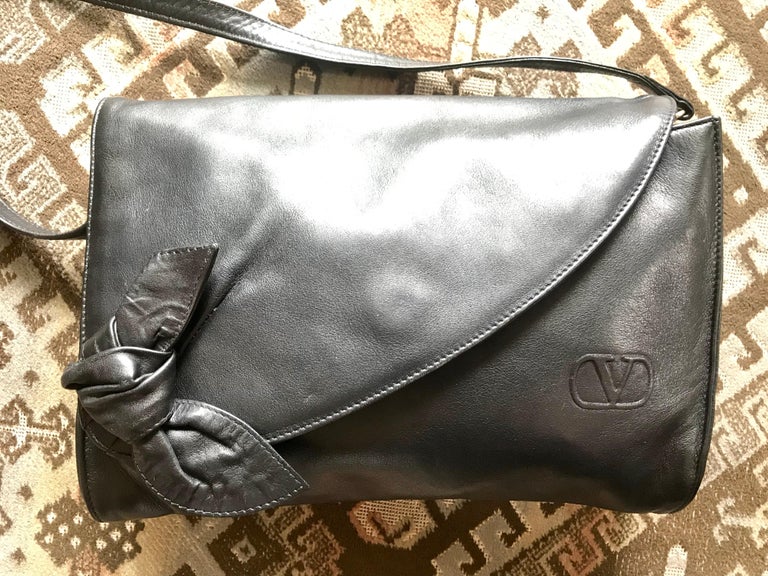 1990s. Vintage Valentino Garavani, Black nappa leather clutch purse, shoulder bag with tied bow, ribbon and V log motif at front.

This is a vintage Valentino Garavani Black nappa leather clutch pouch that can also used as a shoulder bag with a