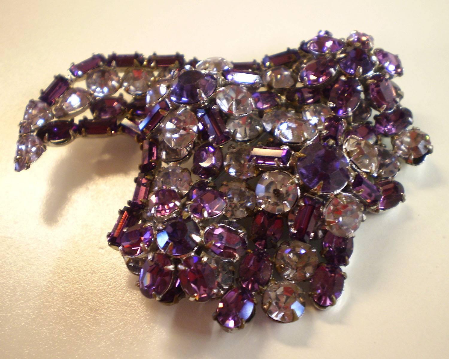 This lovely brooch by Schreiner depicts a stylized cornucopia form, a symbol of luxury and abundance. Gorgeous shades of purple and lilac and many variation of stone shapes and sizes and colors make Schreiner brooches particularly sought after.