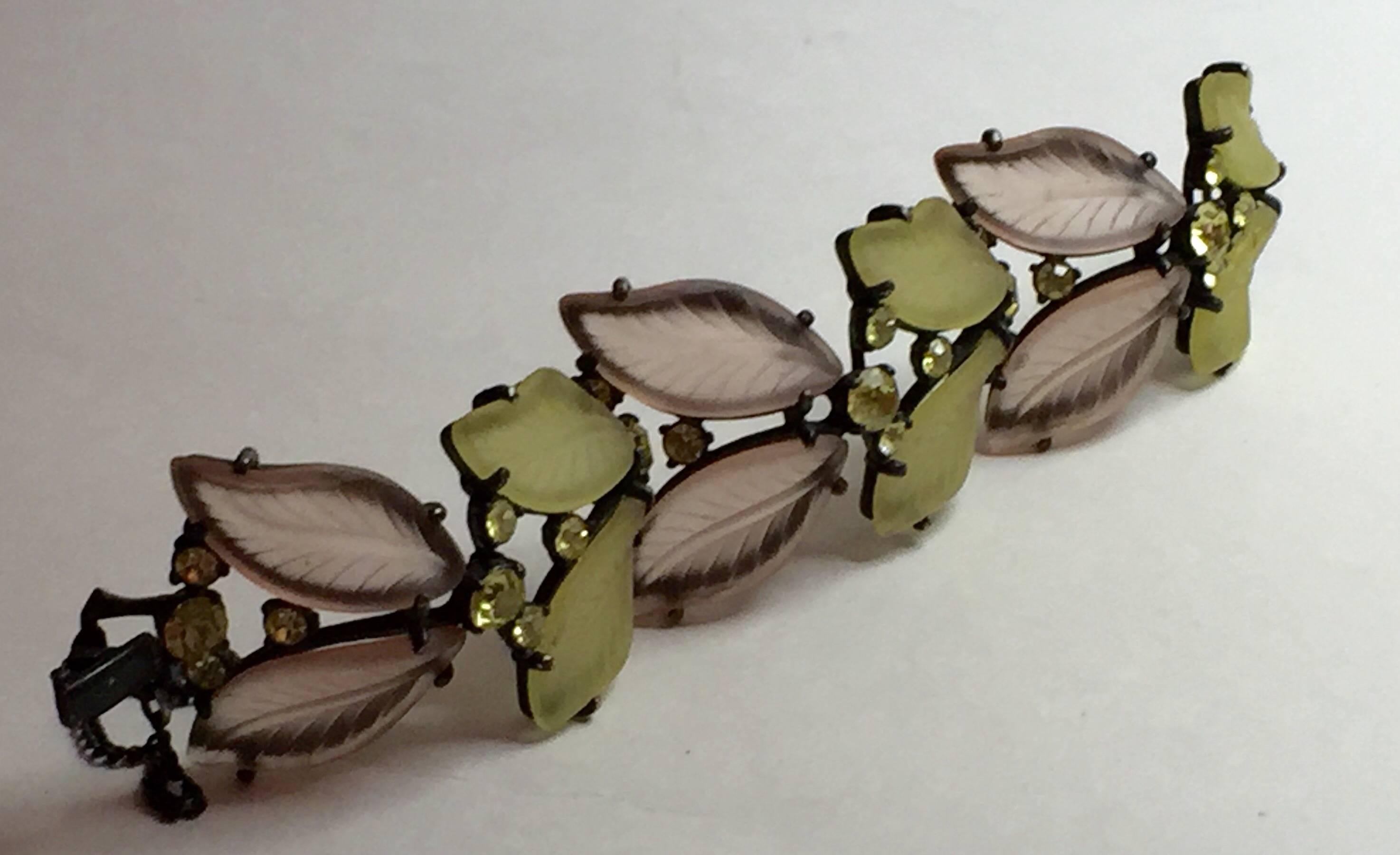 A softly pastel color palette of palest sepia pink and light green set in a darkened metal 'japanned' setting and set off with olivine circular rhinestones, make this Schiaparelli bracelet an unusual design. Reseembling American manufacturer LISNER
