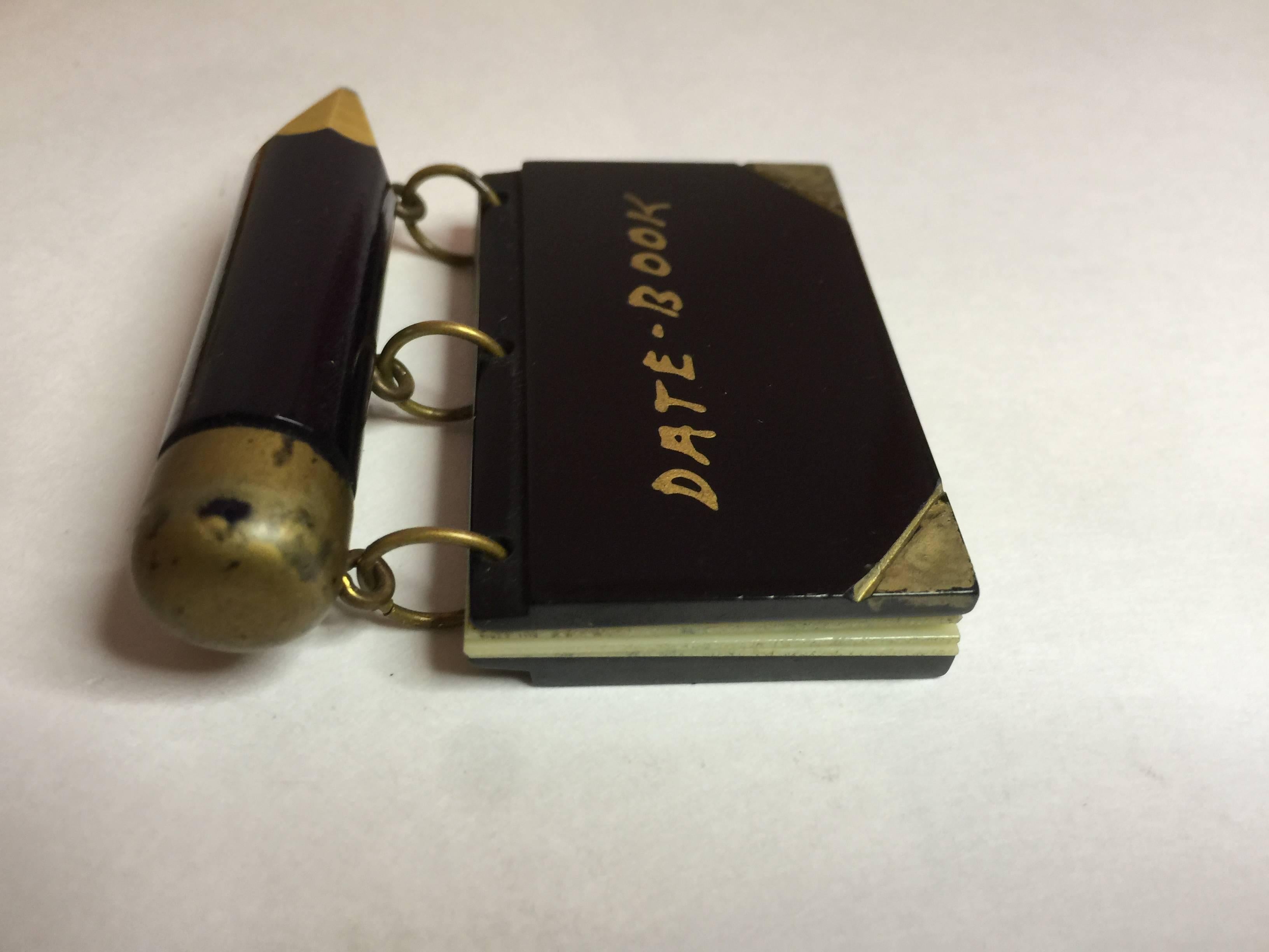 An exceptionally rare figural Bakelite pin, this date book, subcategory from school days similar 'book' pins, is  constructed of a thick painted bakelite pencil as a bar pin on top 1.75