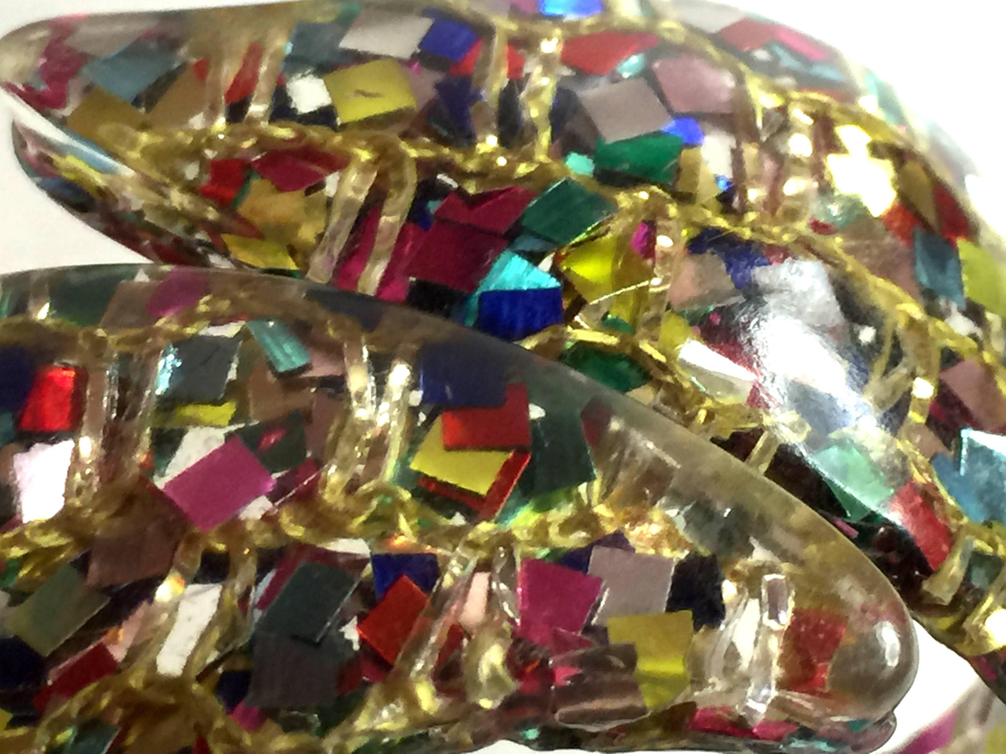 A party on your wrist! Confetti lucite, a thermoset plastic from the 1950s era was used for many kinds of jewelry and purses in the period. This hinged bracelet incorporates the fun and pizazz of multicolored foil confetti flakes in differing shapes