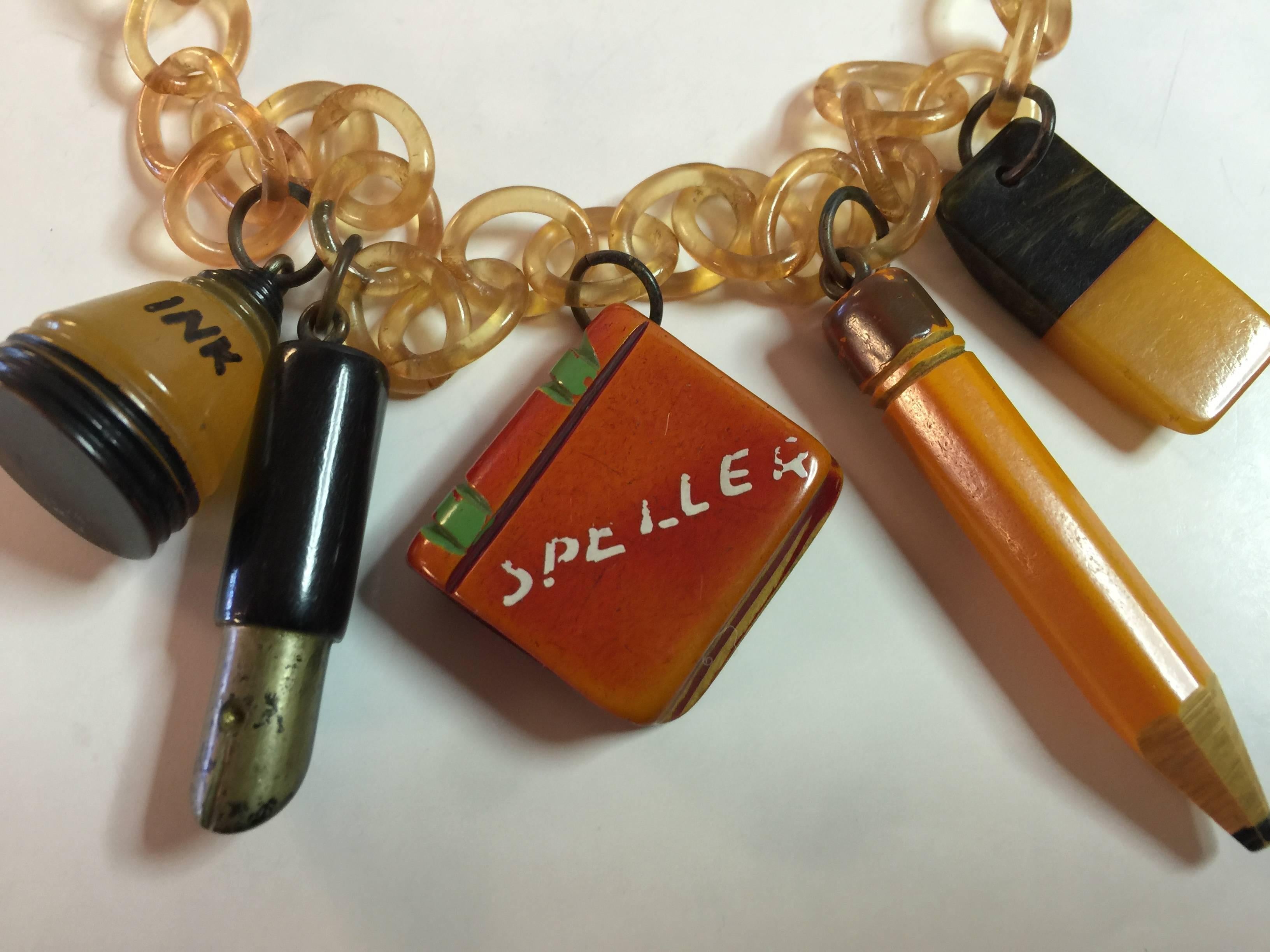 Figural Schooldays Jewelry is highly sought after in the bakelite world A classic necklace comprised of 5 charms suspended by brass or rings from translucent cellulose chain. An ink bottle, old fashioned fountain pen with brass nib, resin washed