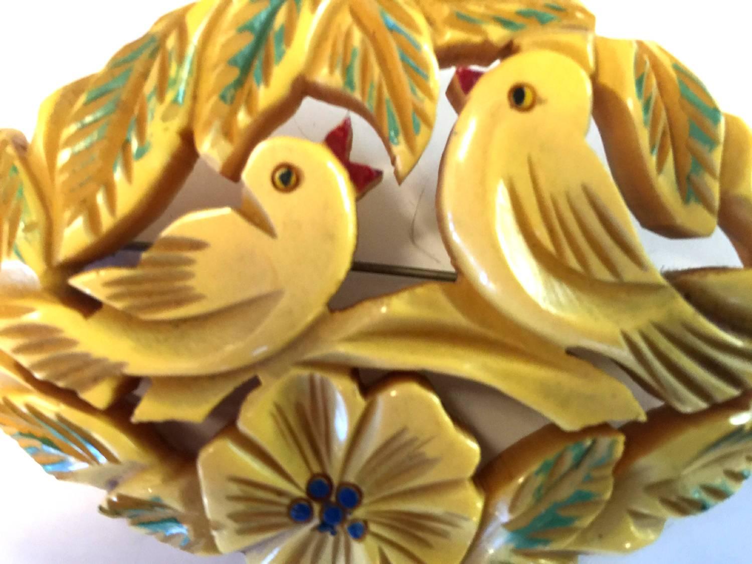 A heavily carved bone bakelite brooch depicts adorable love birds in silhouette beak to beak chirping poses. Surounded by flowers and naturalistic details, the pin has a by hand artisan painted detailing which adds much color and whimsy to the