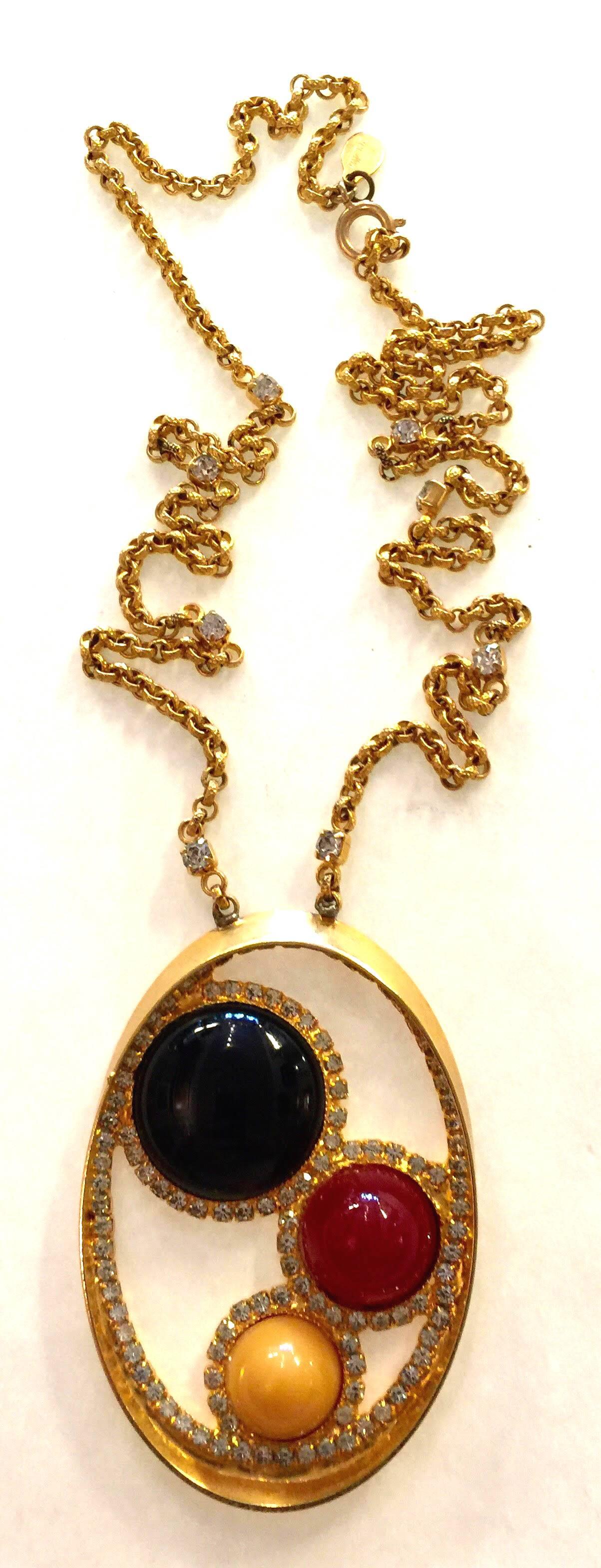 This lovely necklace in pendant style is executed in a rich exquisite plated yellow goldtone finish , a looping lovely oval circlet of diamante detail with 3 variant sized bullet stone cabochons in black, brick rust and buttercream, tonal yet