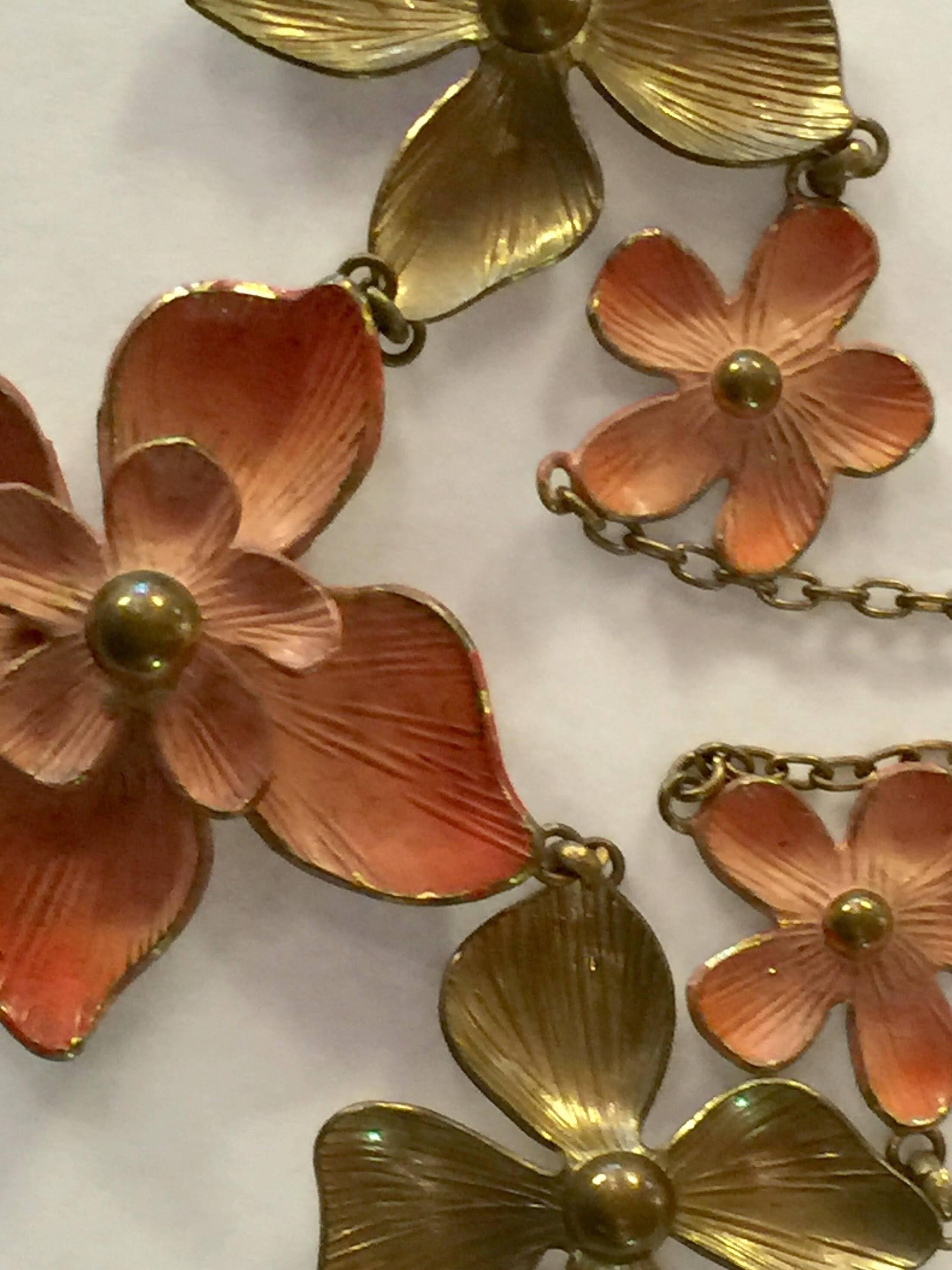 Subtle and sweet, this lovely necklace consists of shiny goldtone backed floral elements, alternating ones of which have been matte gilt with accenting coral sotly enamelled colorized detailing. The brass chain necklace section of the necklace is