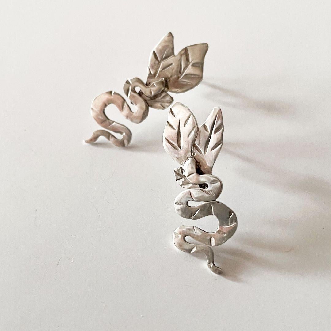 Entièrement fabriquées à la main en argent 925, ces boucles d'oreilles sculpturales représentent un serpent reposant sur des feuilles délicatement texturées. Conçue pour être posée contre le lobe de l'oreille, cette pièce évoque le calme et la force