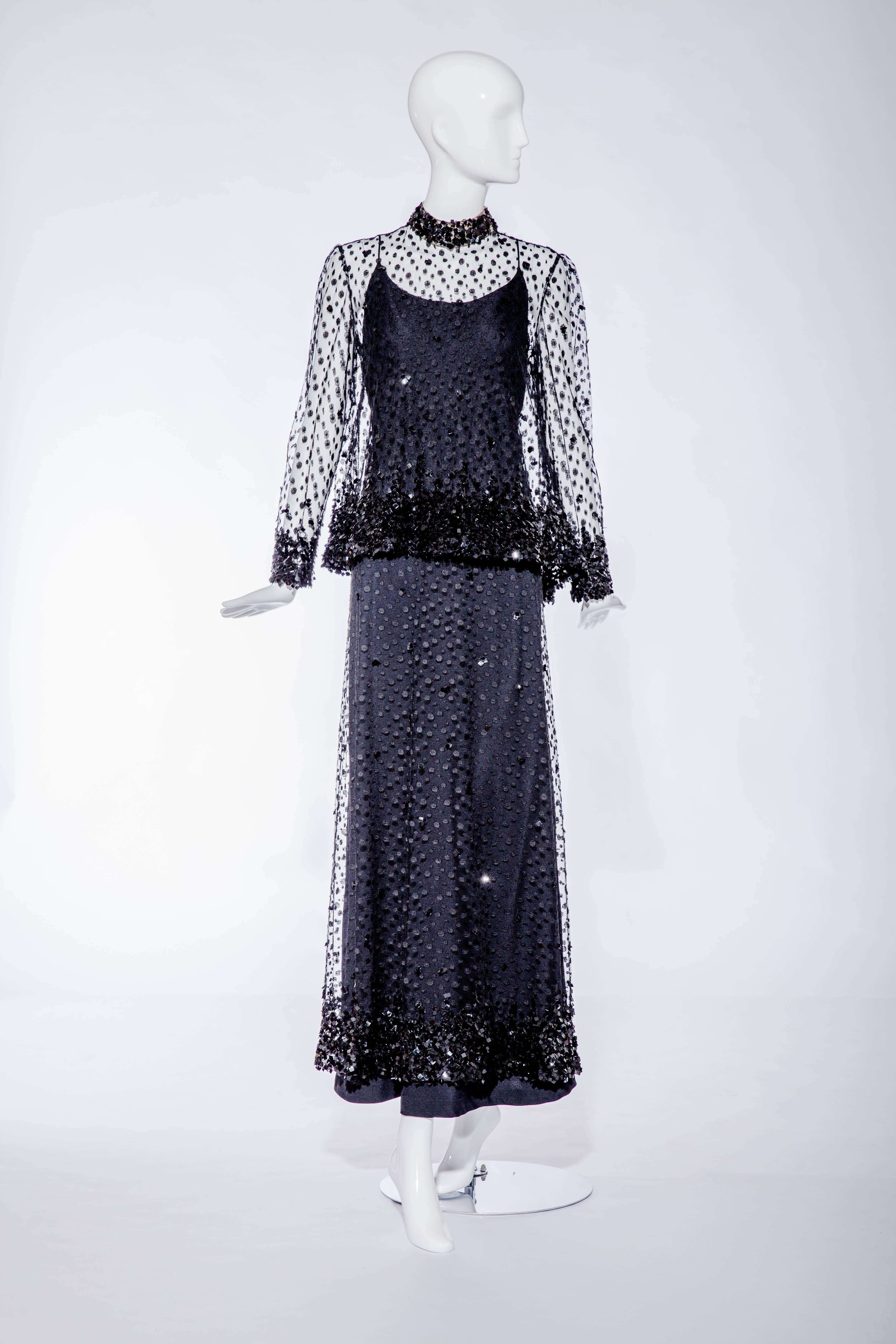 This black lace gown with capelet is a 1970s creation by Alfred Bosand.  The gown has spaghetti straps and is constructed with black silk crepe that has an overlay of lace that is paillette-embellished.  The lace net is painstakingly covered with