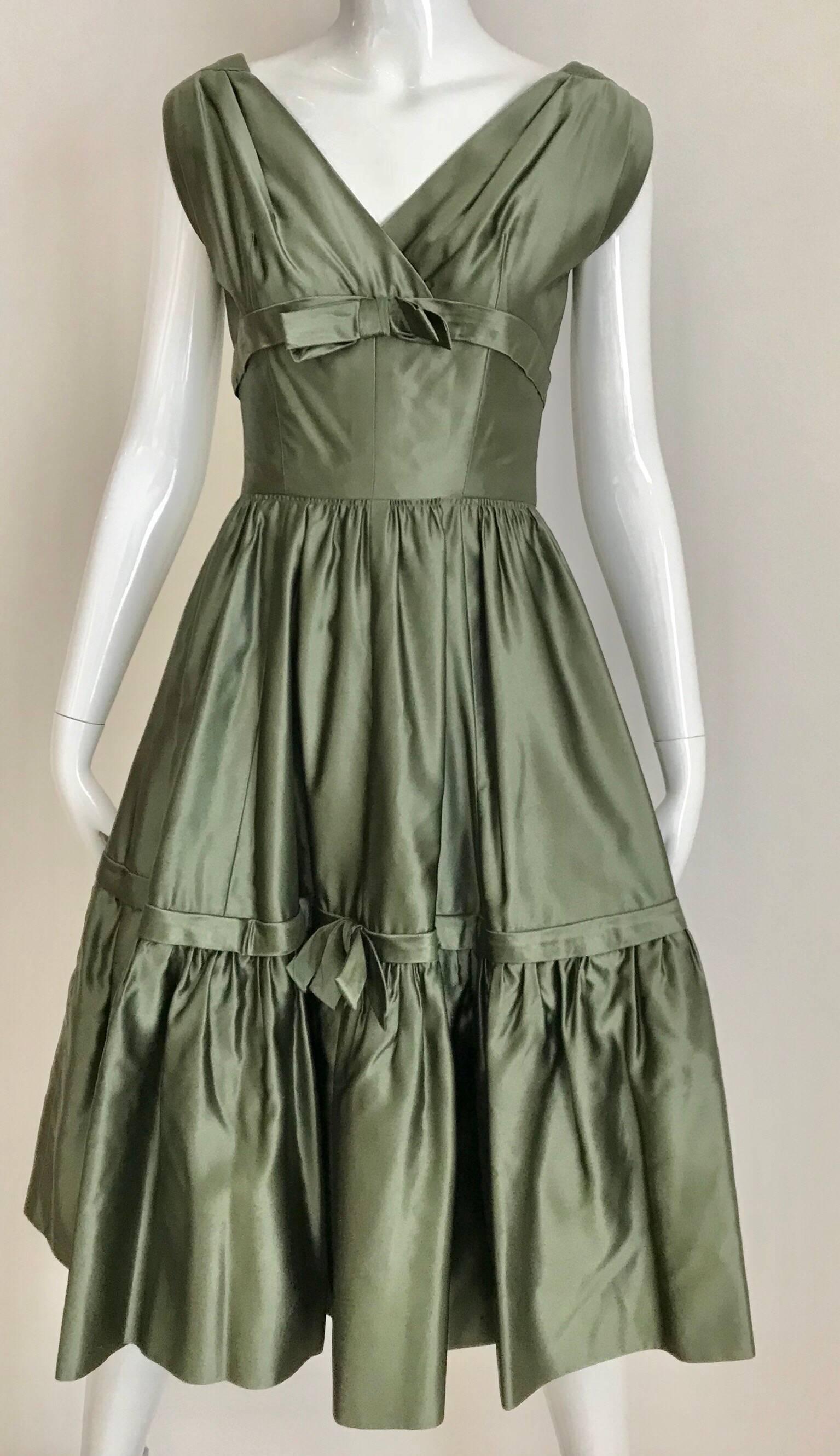 Classic 1950s Christian Dior Boutique - New York Cocktail Dress.
Beautiful moss green silk satine V neck dress with bows and cap sleeves. Dress has thin crinoline underneath. 
Fit size US 2/4 ) See Measurement:
Bust: 32 inches/ Waist: 24 inches