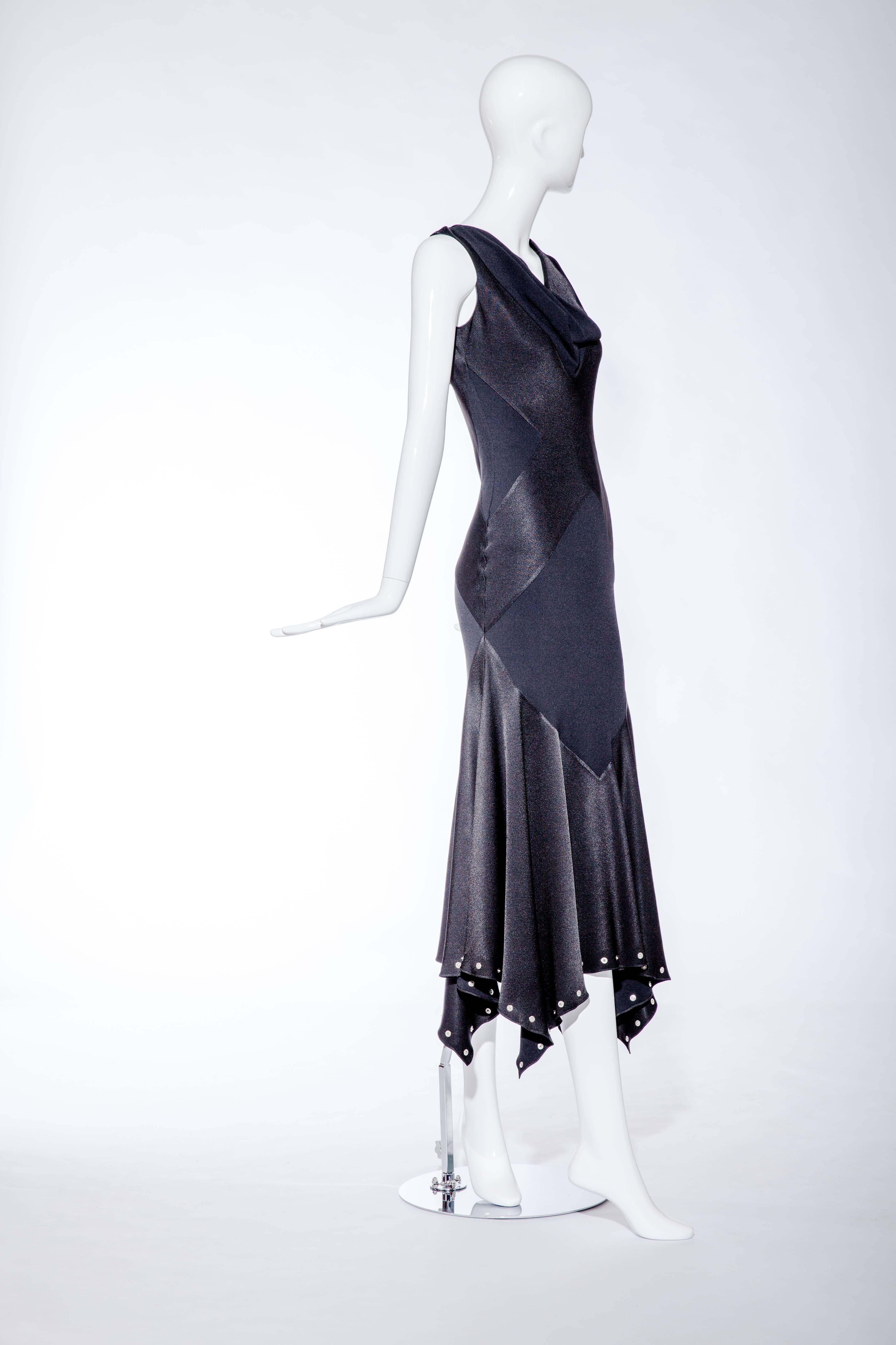 This 1990’s John Galliano black silk charmeuse dress has a biased cut and is inspired by a 1930’s design.
The hemline is studded with silver grommets and there is a subdued “X” pattern on the front and back of the dress and the draping of the cowl