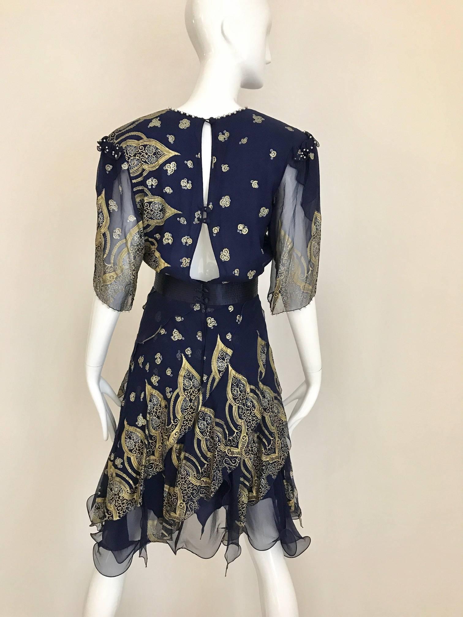 This 1980s blue Zandra Rhodes silk chiffon cocktail dress is highlighted with a gold and silver Indian print etched with sequins. The collar, shoulders and sleeve cuffs are edged with small pearls. The lower portion of the dress has a multi-layered