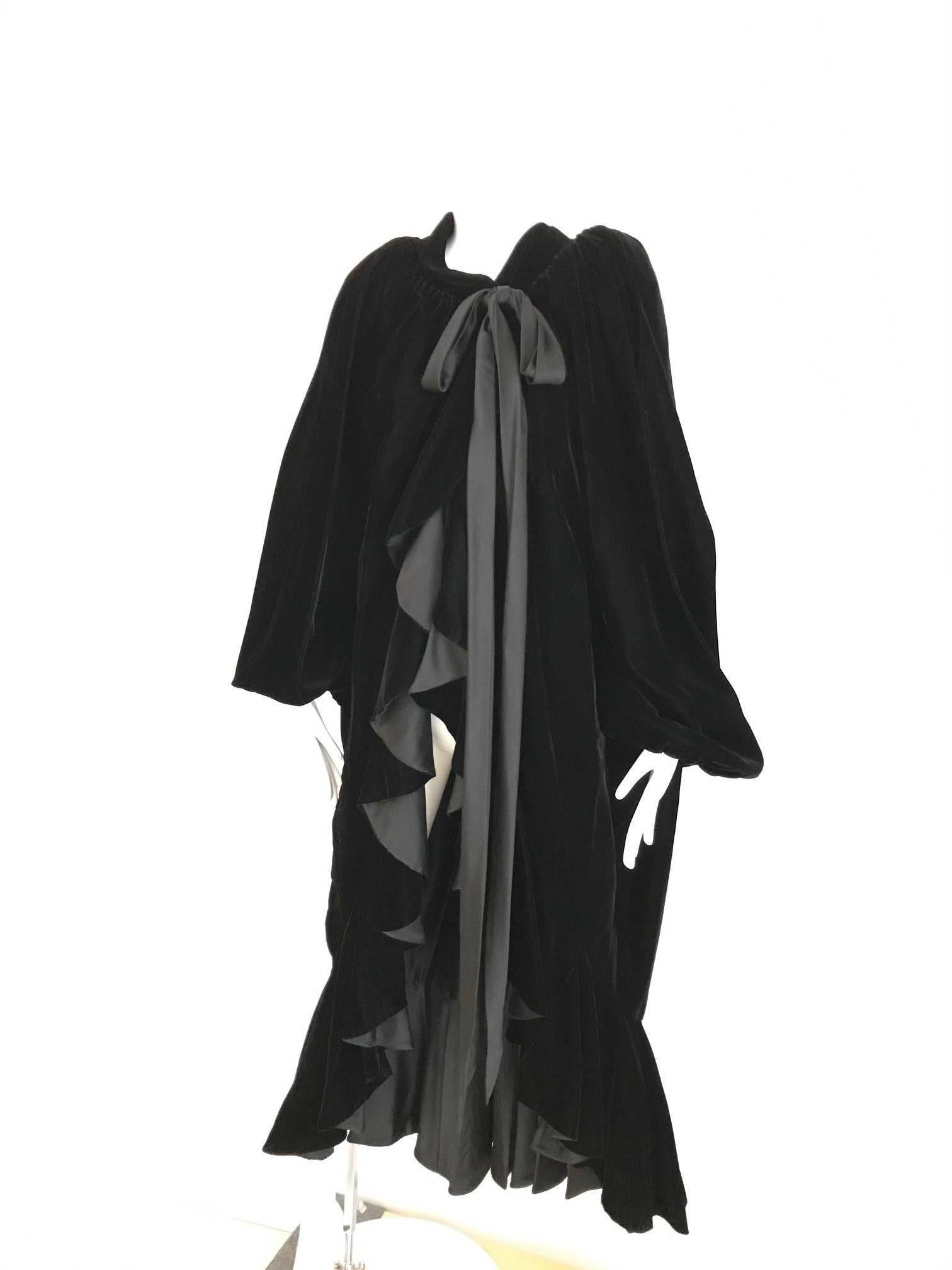 This rare 1980's Yves Saint Laurent black velvet evening coat /cape is the epitome of old world elegance. The design incorporates mild shoulder pads and large billowy sleeves that create the illusion of a cape. There is a very long, thin satin sash
