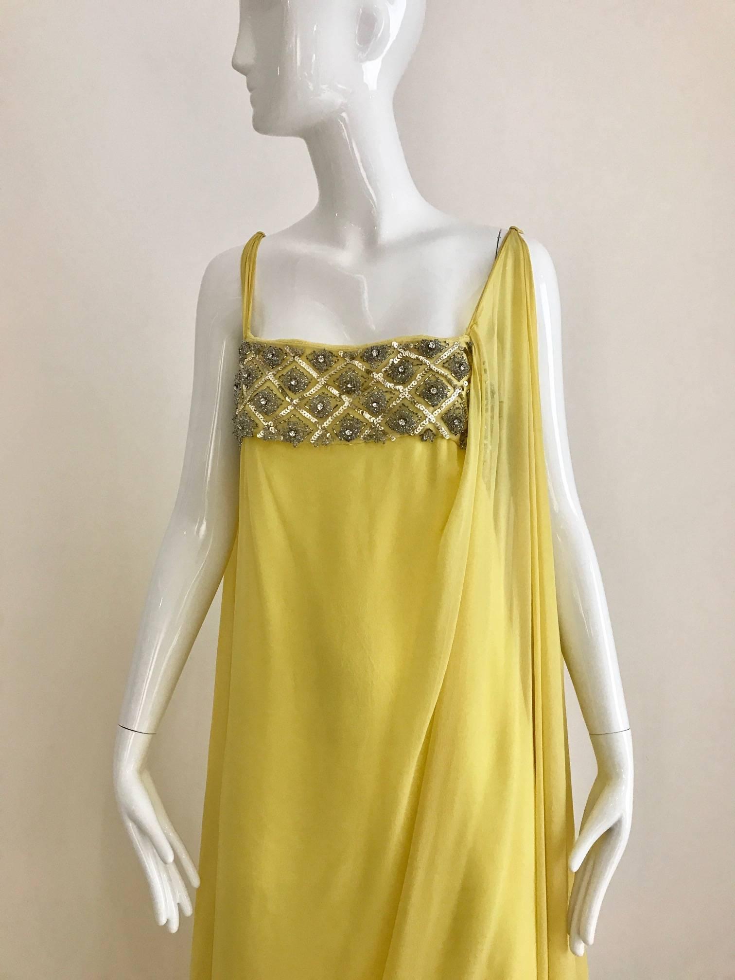 This vintage 1960s yellow silk chiffon Grecian sleeveless gown is the epitome of Grace Kelley elegance. The bodice is highlighted with rhinestones and silver sequins, while the the right shoulder has a long train attached at the top of the shoulder