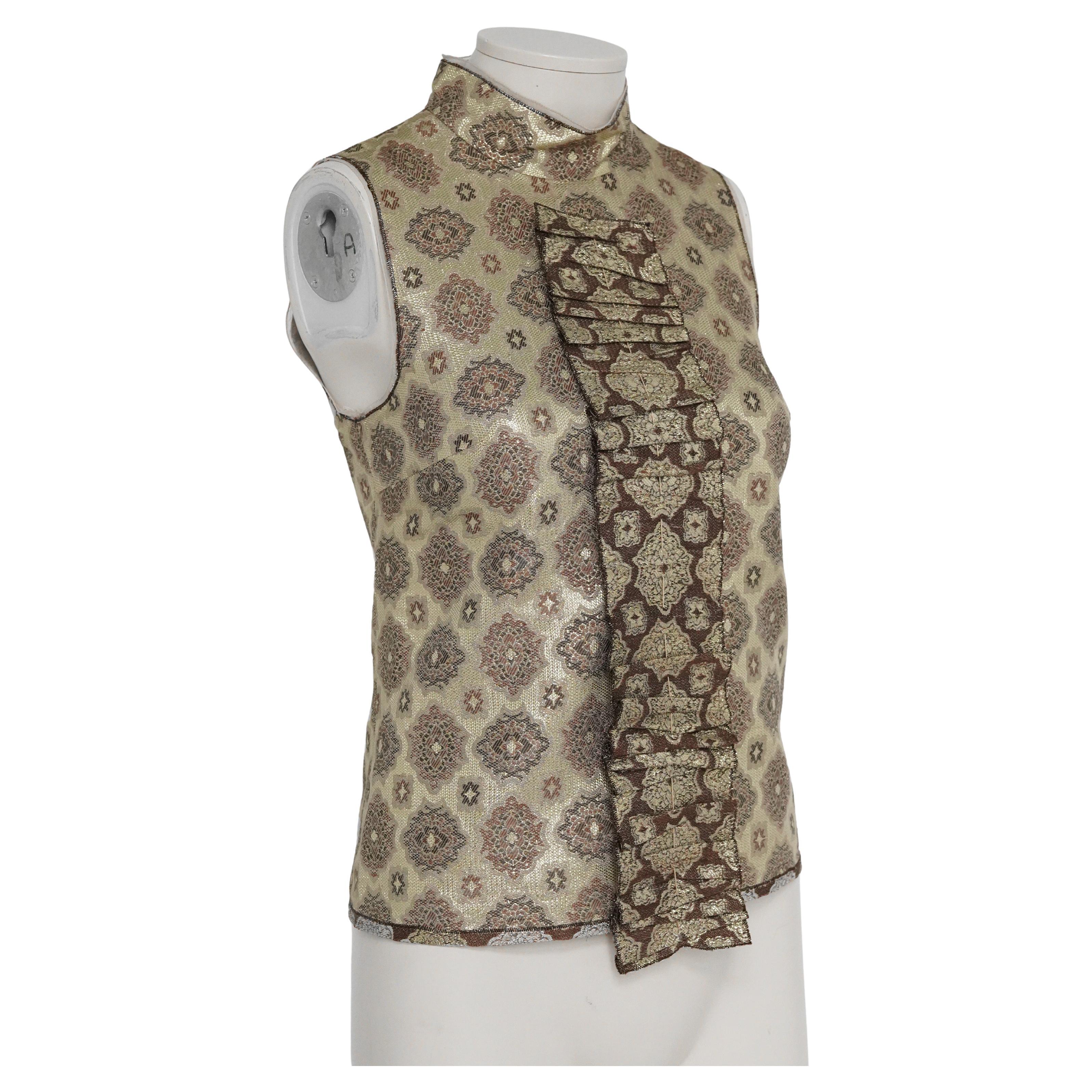 Voici une blouse sans manches en lamé doré à motifs décoratifs de Prada S/S 2002, ornée d'un large panneau à volants. La collection S/S 2002 était axée sur une nouvelle perspective du lamé - déconstruit et restructuré pour créer une image somptueuse