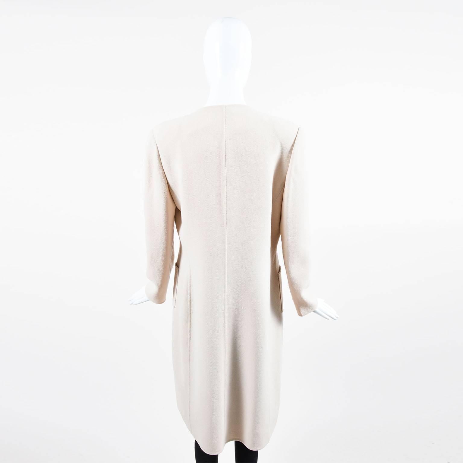 Beautiful, minimalistic duster jacket. Beige woven crepe with complementing taupe silk panel. Long sleeves. Collarless; rounded neckline. Hemline hits below the knee. Square pockets at hips. Padded shoulders. Concealed front button closures.