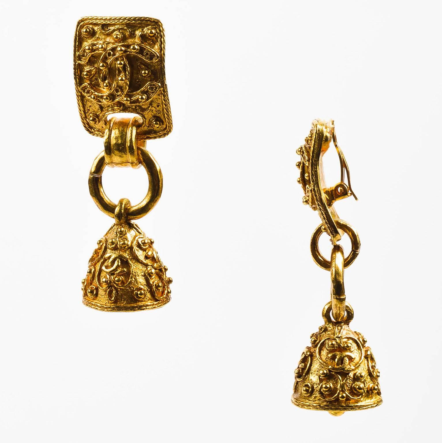These vintage Chanel earrings combine ornate design & whimsical character; design from the 1994 Fall Collection. Gold tone metal with beaded texture and iconic 'CC' logos. Rectangular base holds a graceful, ringing bell. Clip on backs.